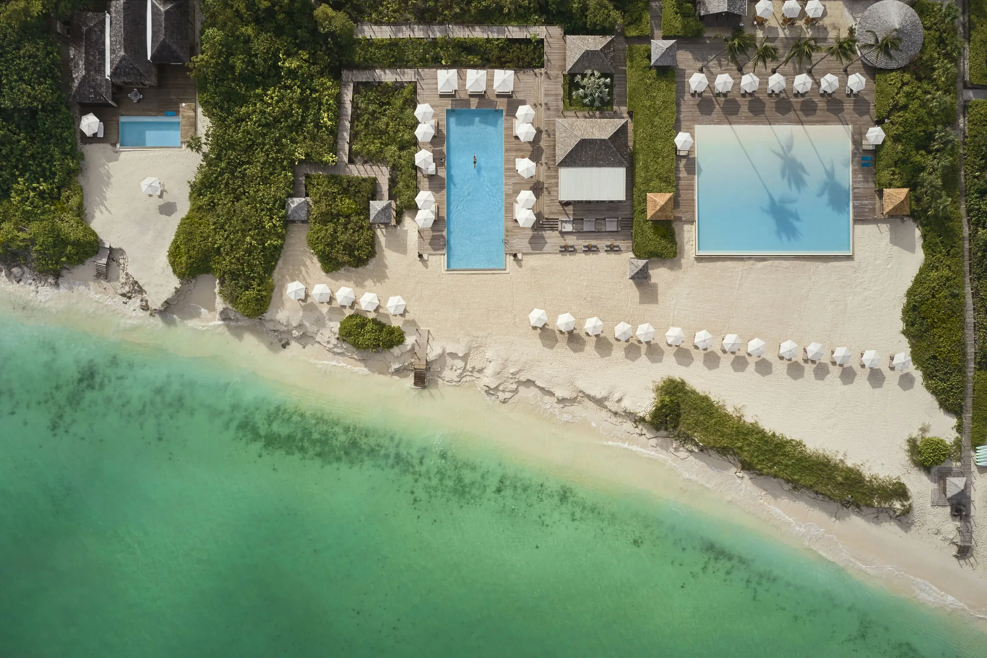 Two beachfront pools and rows of umbrellas sit beside clear water at COMO Parrot Cay.