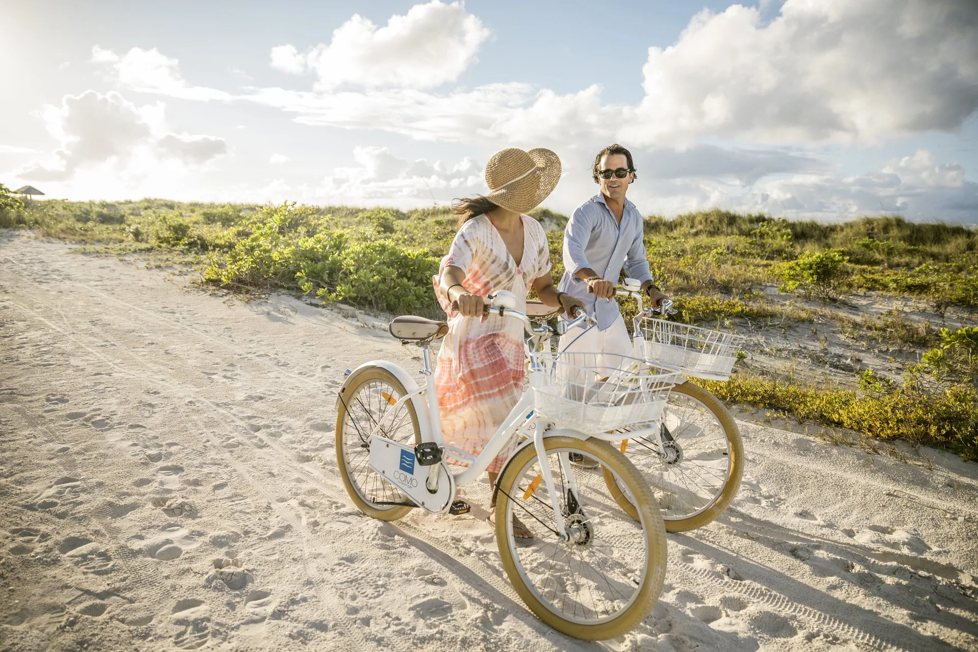 Two guests ride white bicycles along a sandy path at COMO Parrot Cay.