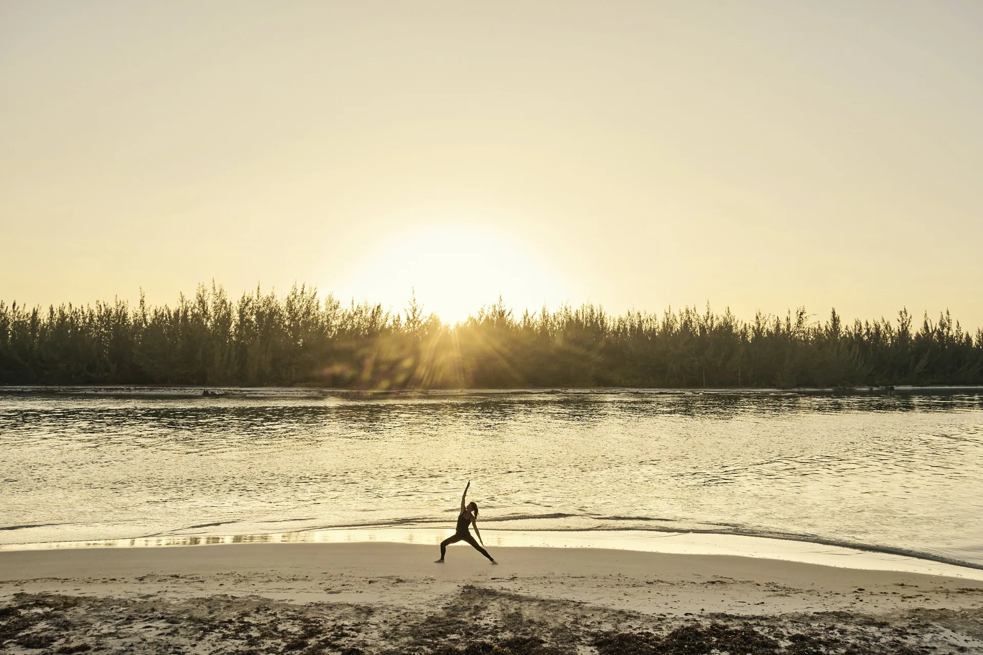 Beach yoga at COMO Parrot Cay with a person posing near the shoreline at sunrise.