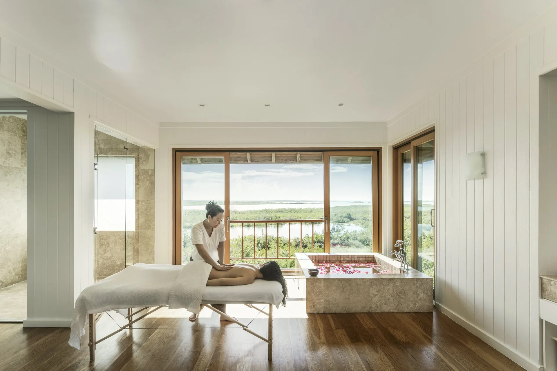 Spa treatment room at COMO Parrot Cay with massage bed, soaking tub, and wide water views.