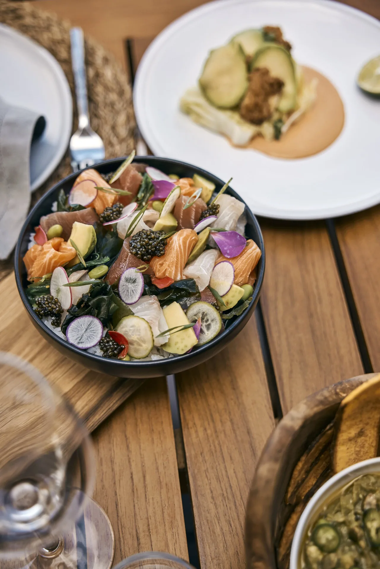 Colorful sashimi bowl and plated dishes on a wooden table at COMO Parrot Cay.