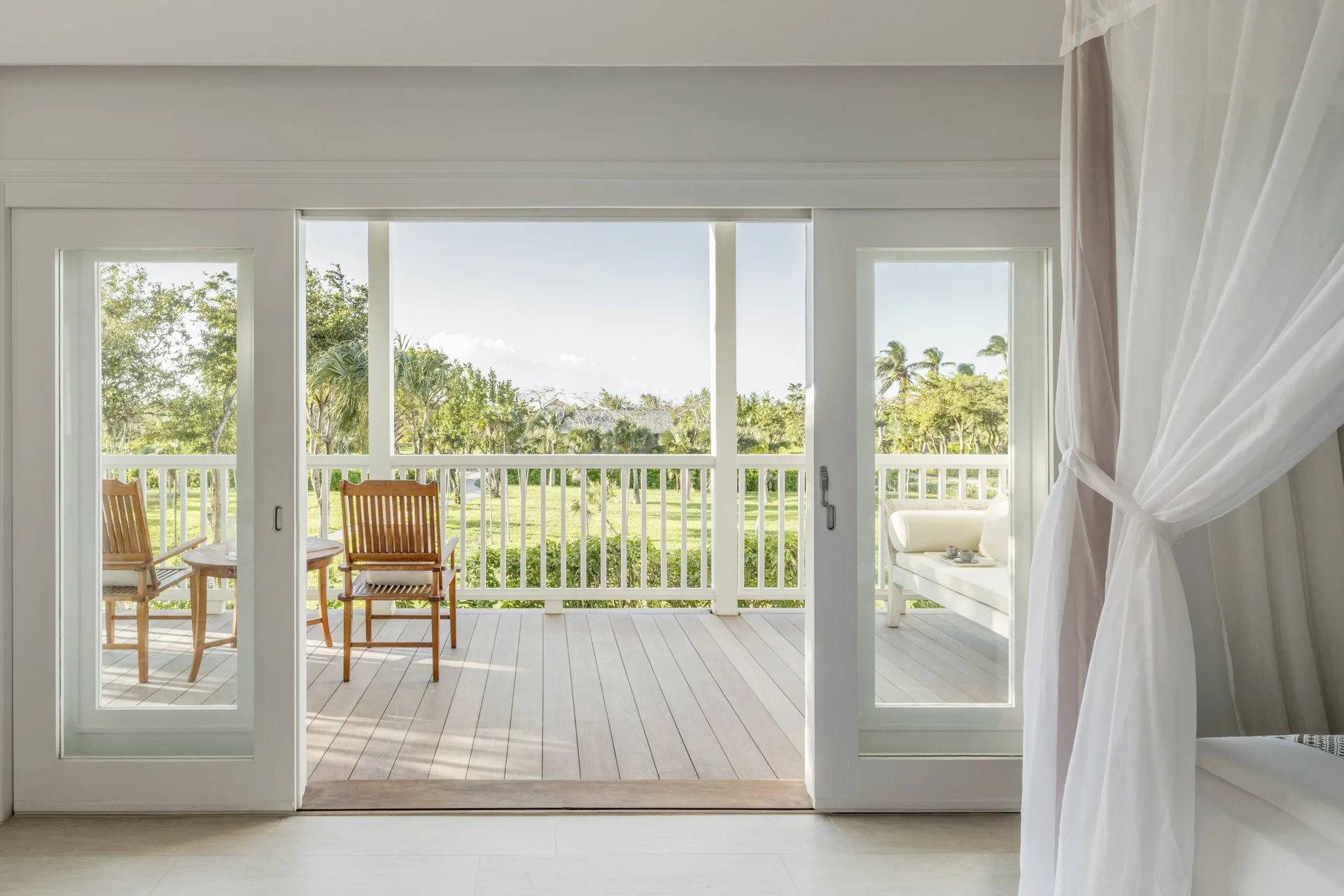 Terrace Room balcony at COMO Parrot Cay seen through sliding doors beside a draped bed.