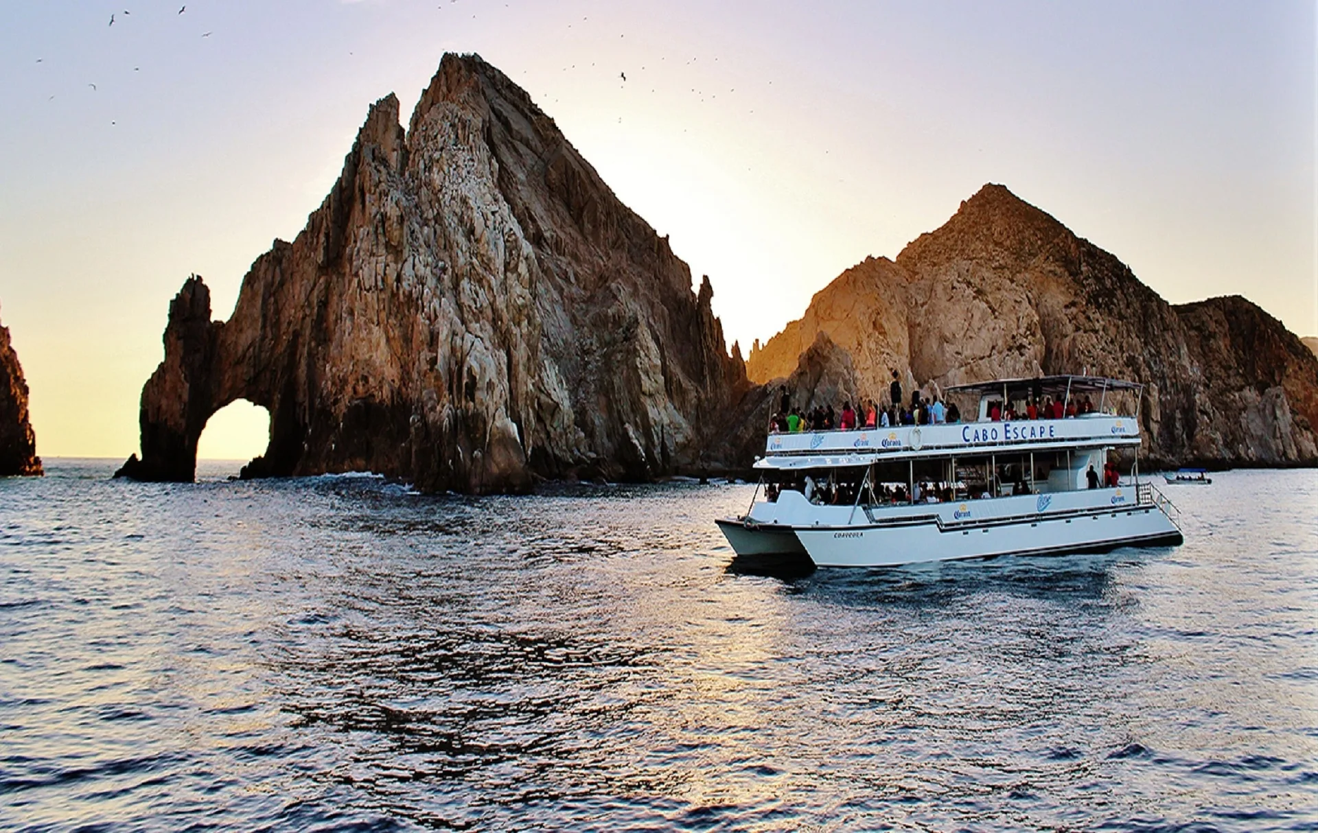 Tour boat passing the rock arch at sunset near Corazón Cabo.