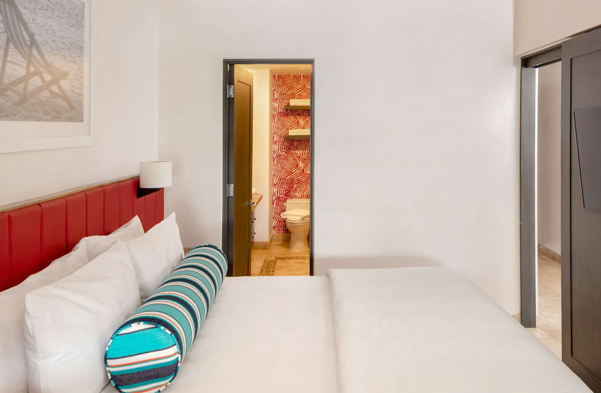 One Bedroom Deluxe king bed with red headboard and bathroom doorway at Corazón Cabo.