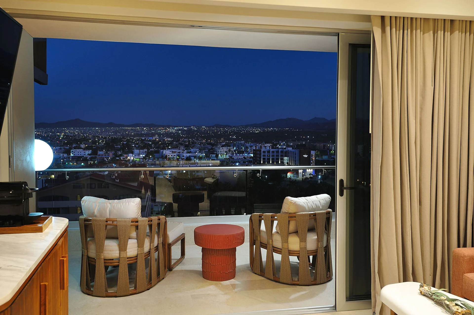 Balcony chairs face evening city lights from an Infinity Sunset View room at Corazón Cabo.