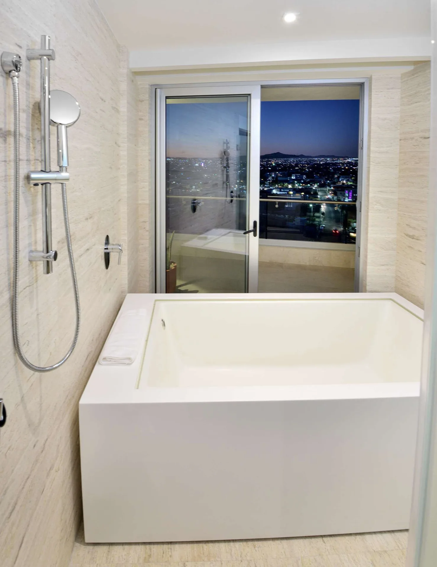 Bathroom soaking tub and shower fixture with nighttime balcony view at Corazón Cabo.