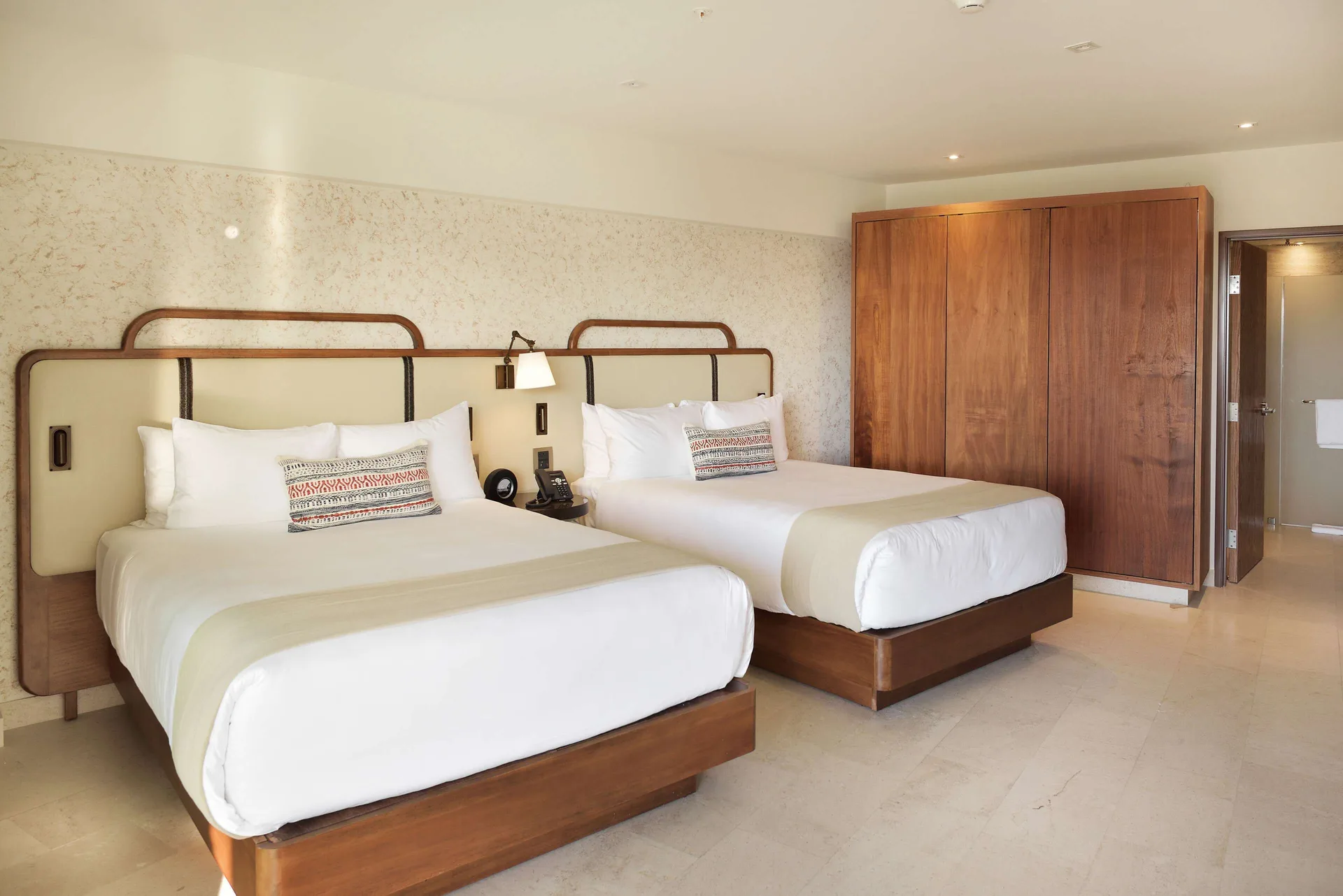 Bedroom with two beds, wood wardrobe, and bathroom doorway in a suite at Corazón Cabo.