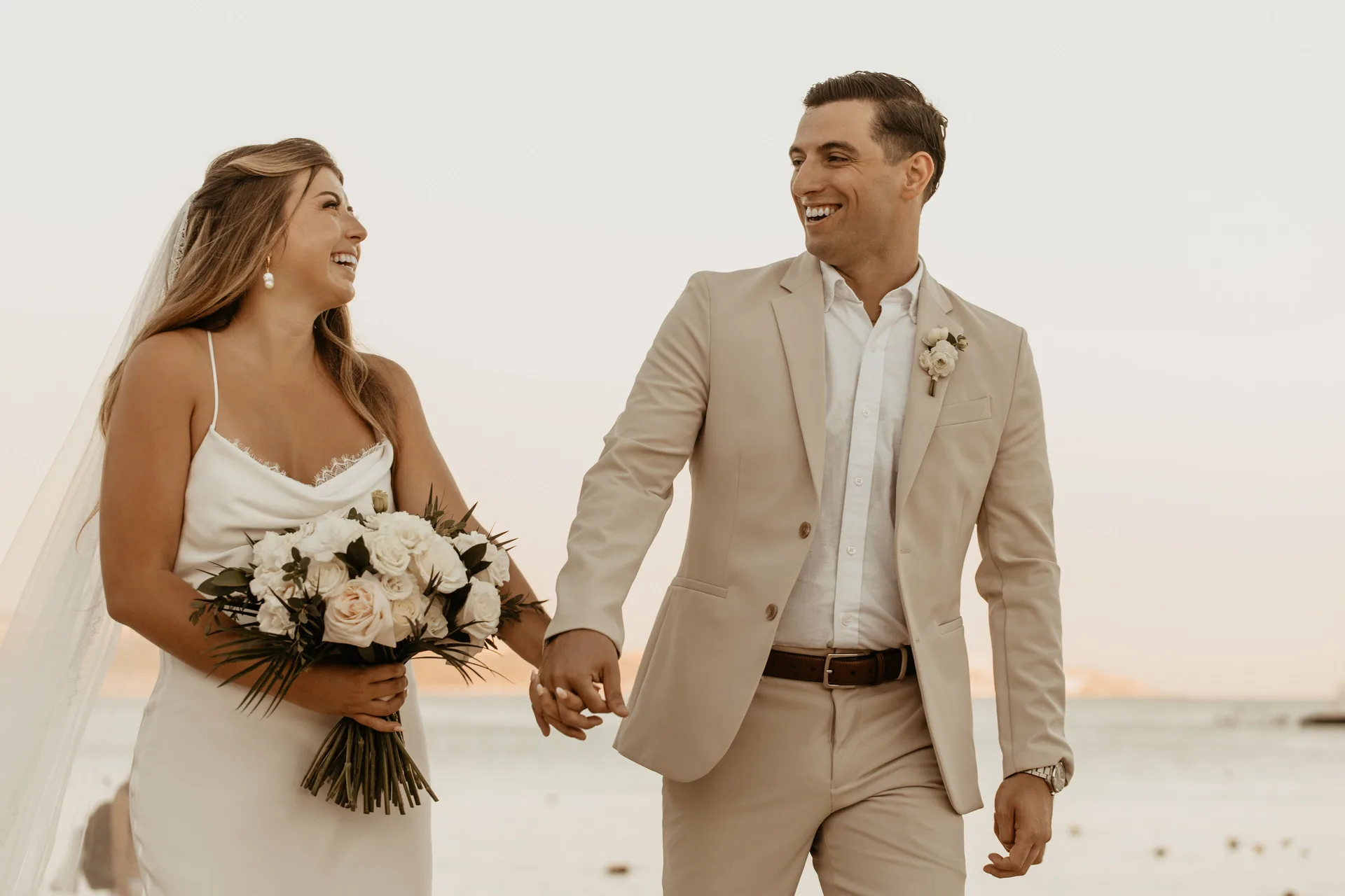 Bride and groom holding hands by the beach at Corazón Cabo.
