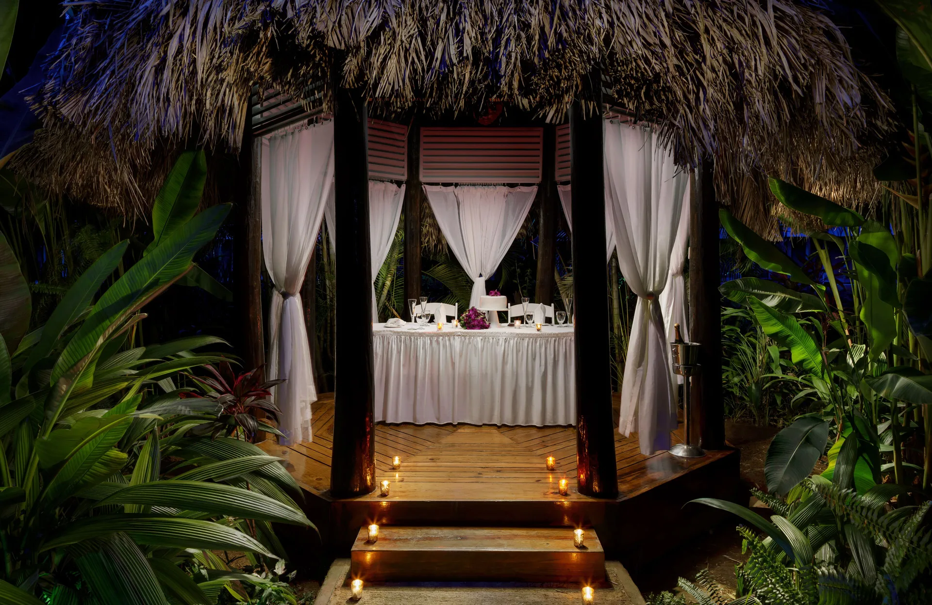 Candlelit thatched gazebo dining setup in tropical gardens at Couples Negril.