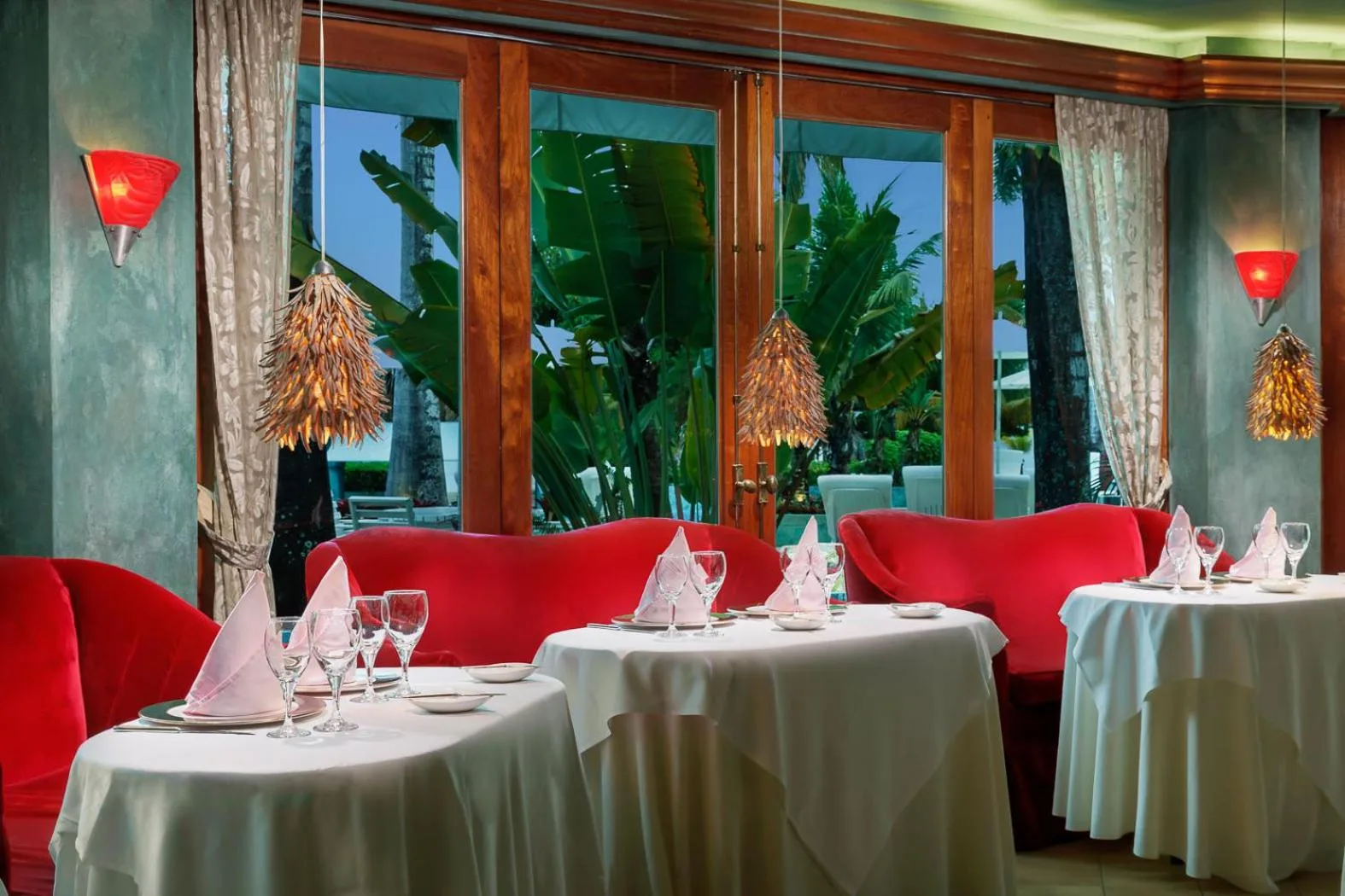 Intimate dining room with red banquettes and set round tables at Couples Negril.