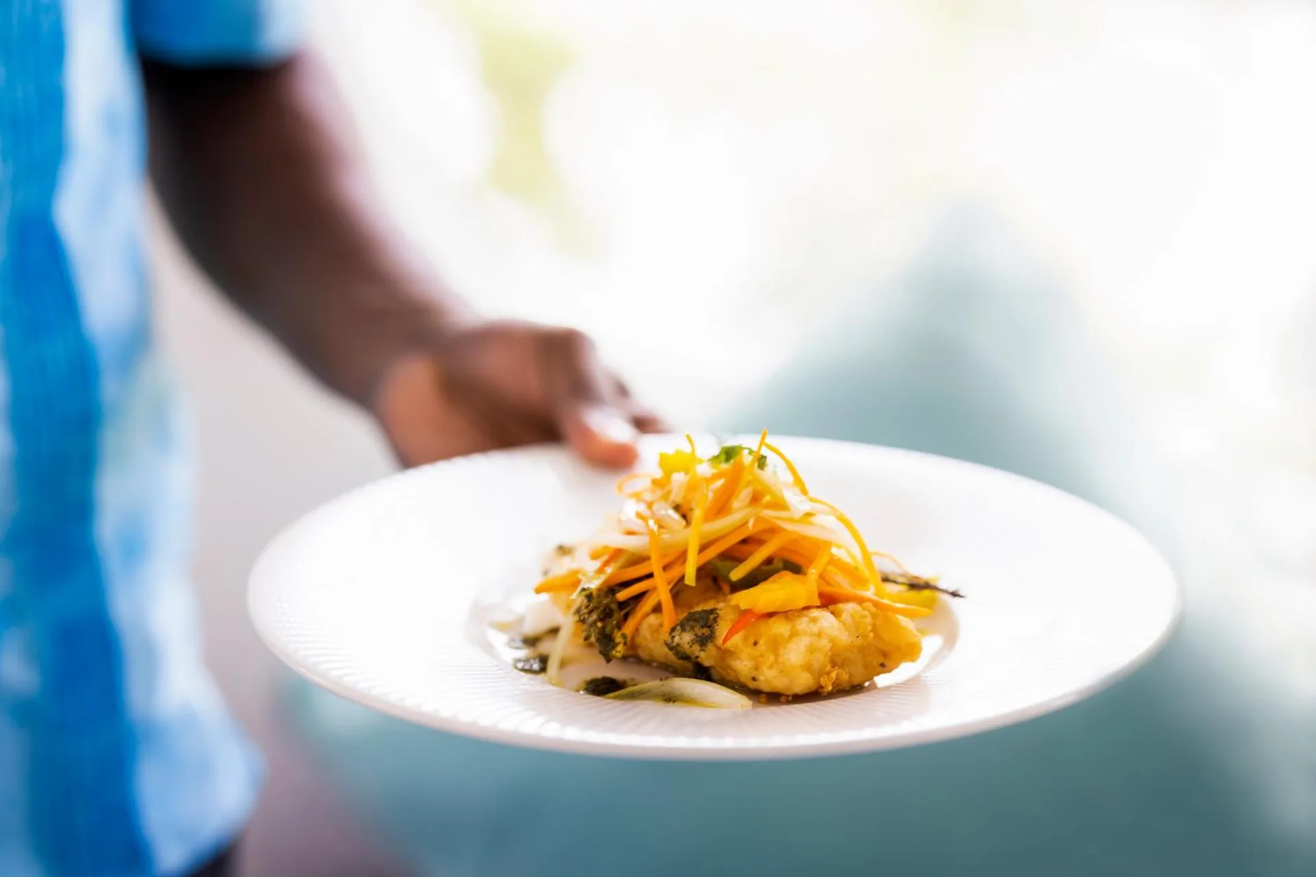 Server carrying a plated entrée with colorful garnish at Couples Negril.
