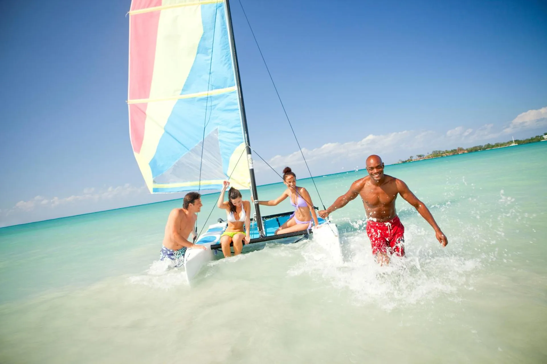 Guests wade beside a small sailboat in clear turquoise water at Couples Negril.