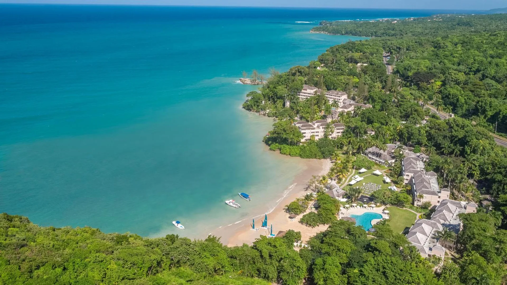 Wide aerial view of the resort coastline, beach, pool, and forest at Couples Sans Souci.