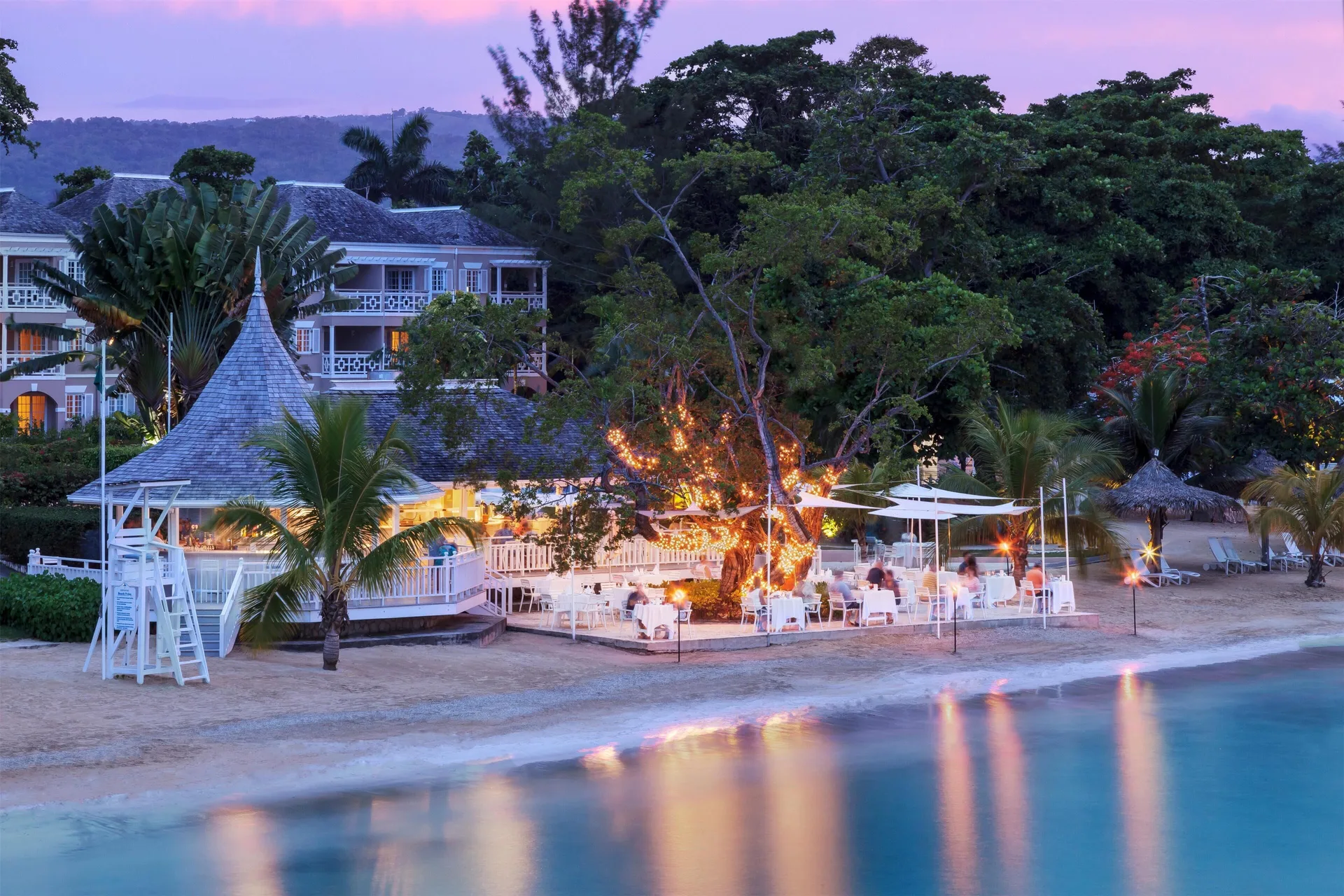 Beachfront dining area glowing at dusk beside the water at Couples Sans Souci.