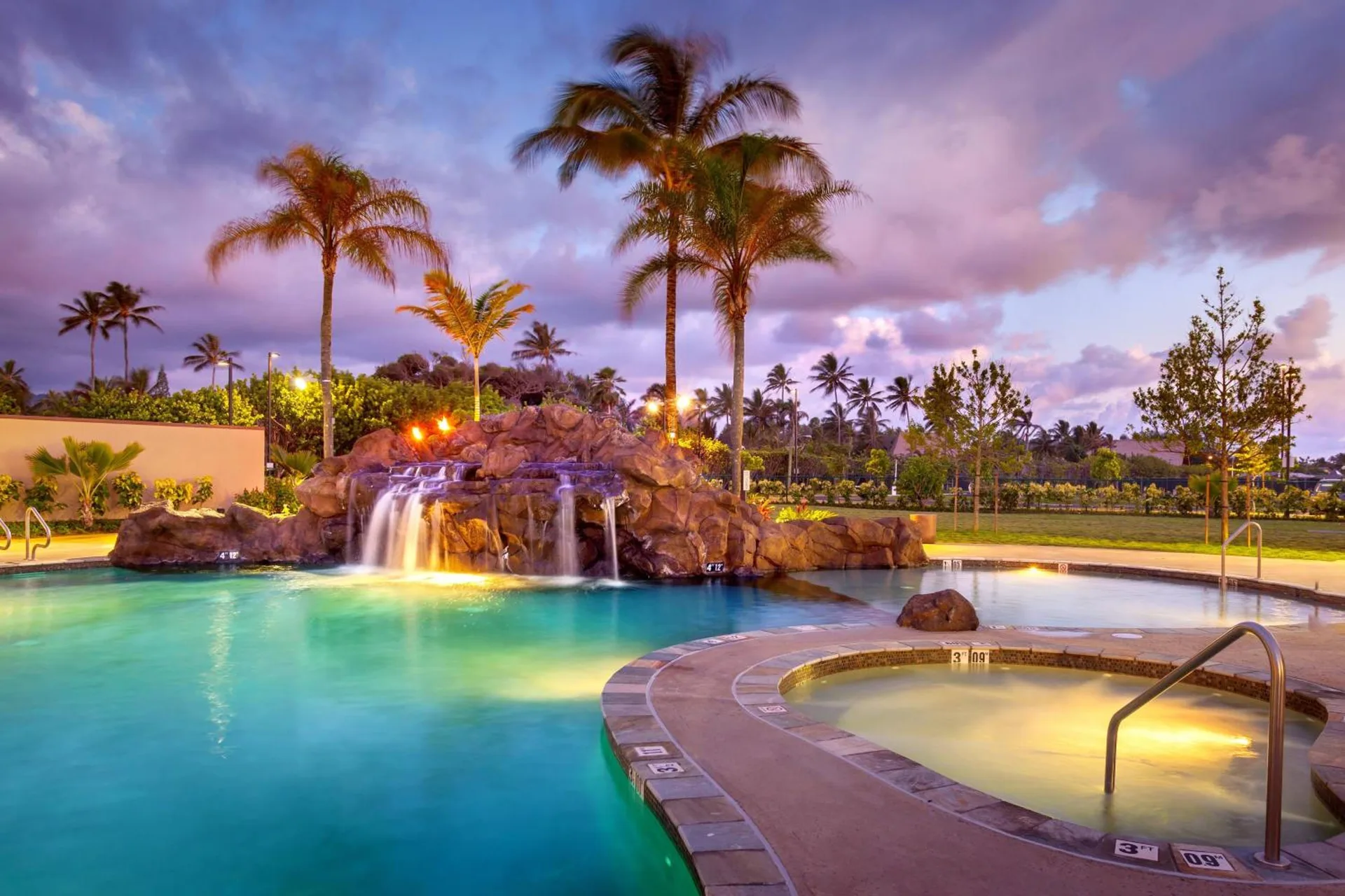 Pool and hot tub with waterfall and palm trees at dusk at Courtyard Oahu North Shore.