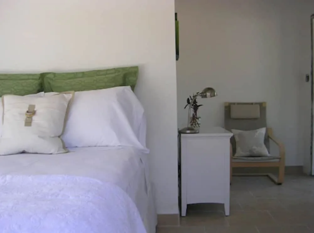 Guest room bed and chair at Cruz Bay Boutique Hotel with white linens and green pillows.