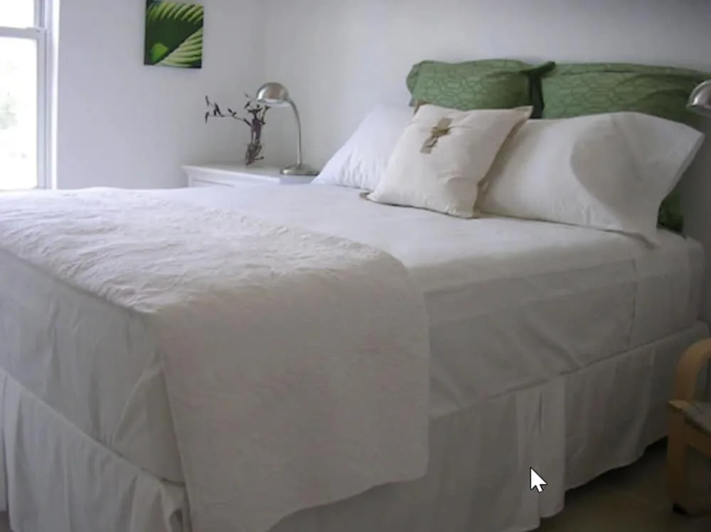 Guest room bed with white linens, green pillows, and bedside lamp at Cruz Bay Boutique Hotel.
