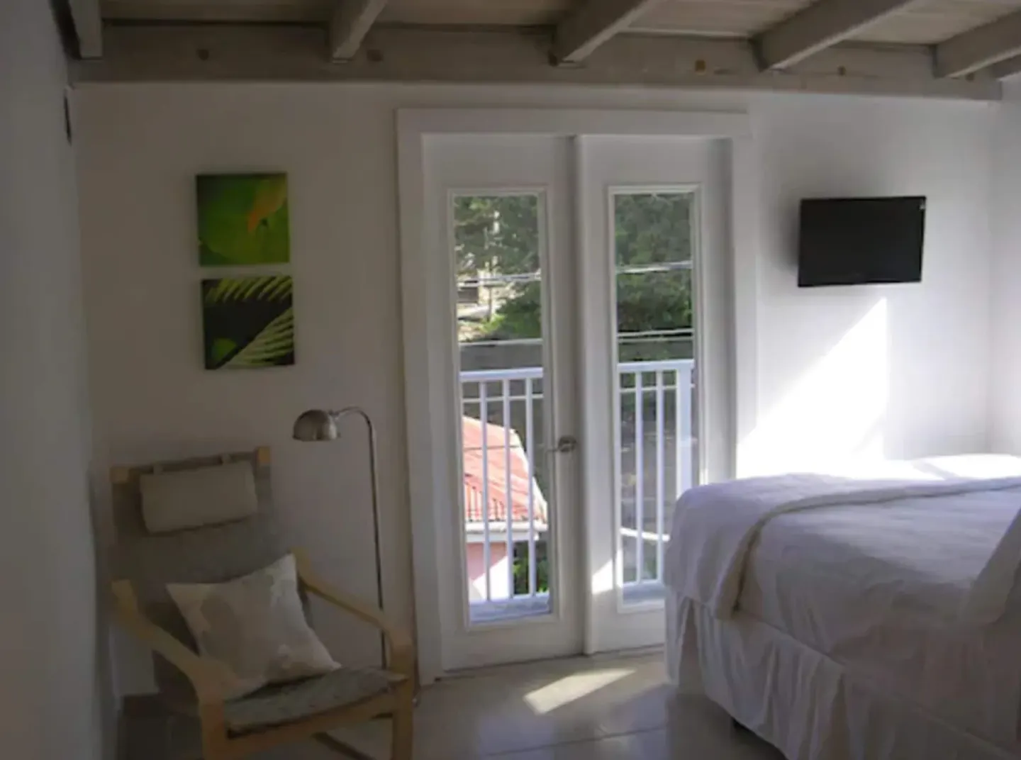 Standard Room balcony doors, bed, and wall-mounted TV at Cruz Bay Boutique Hotel.