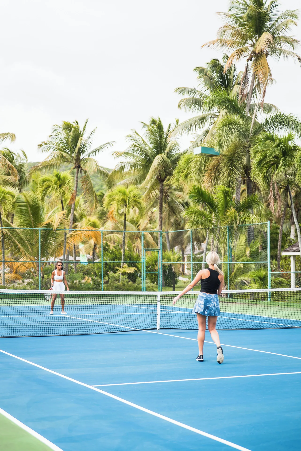Two guests play tennis on a blue court surrounded by palms at Curtain Bluff Resort.