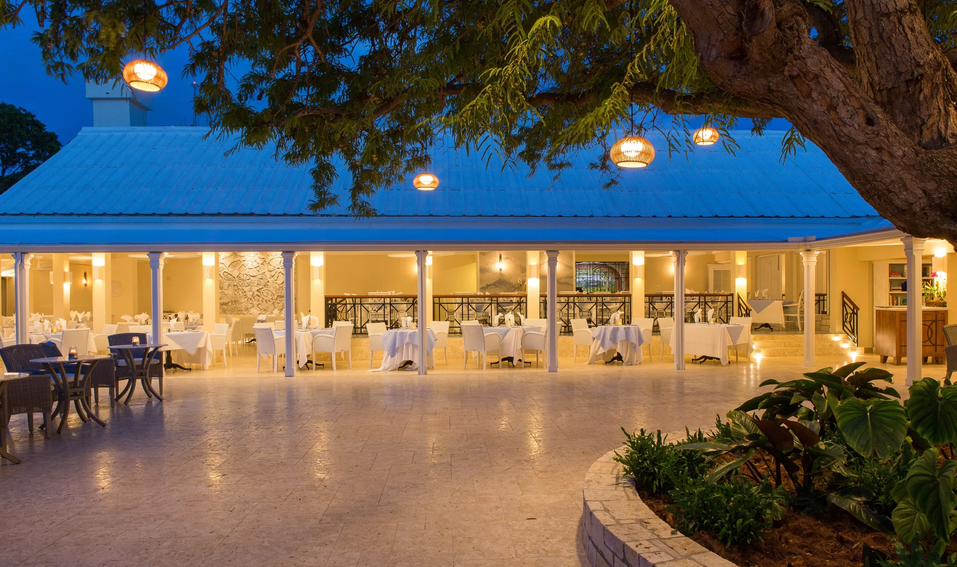 Open-air restaurant terrace set for dinner at Curtain Bluff Resort under evening lights.