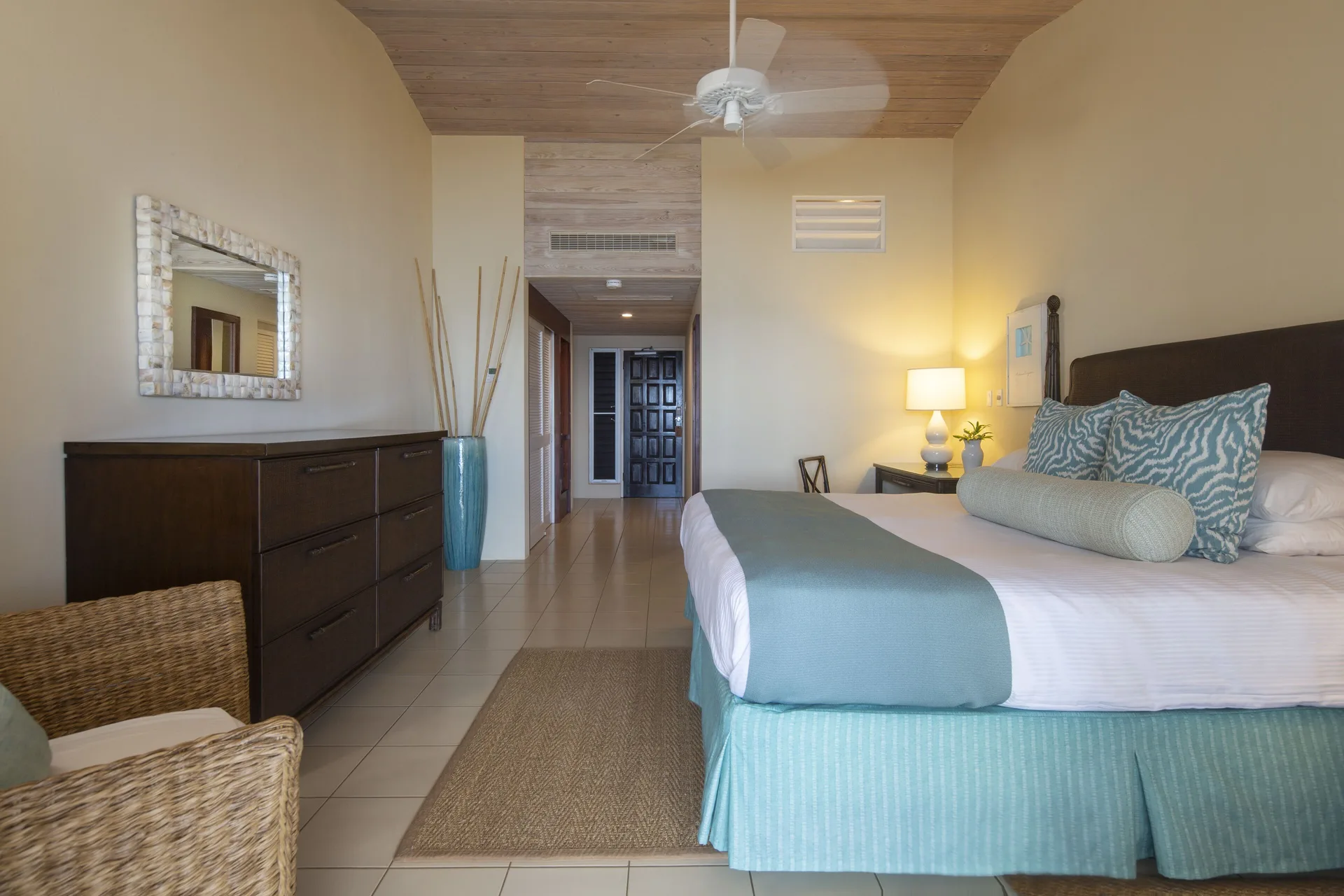 Deluxe Room Beach View king bed with dresser, chair, and entry hall at Curtain Bluff Resort.