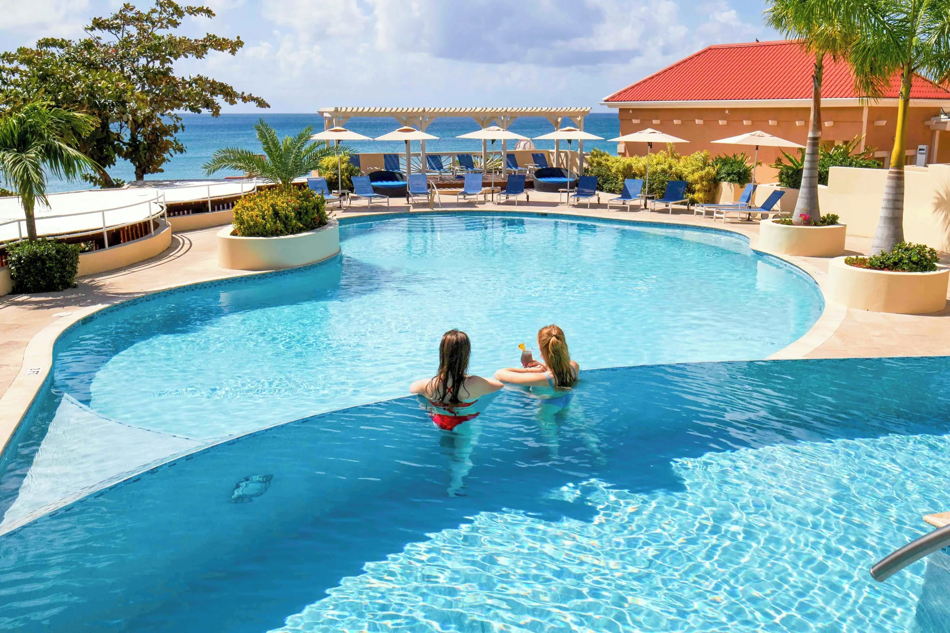 Two guests relaxing in a large pool at Divi Little Bay Beach Resort.