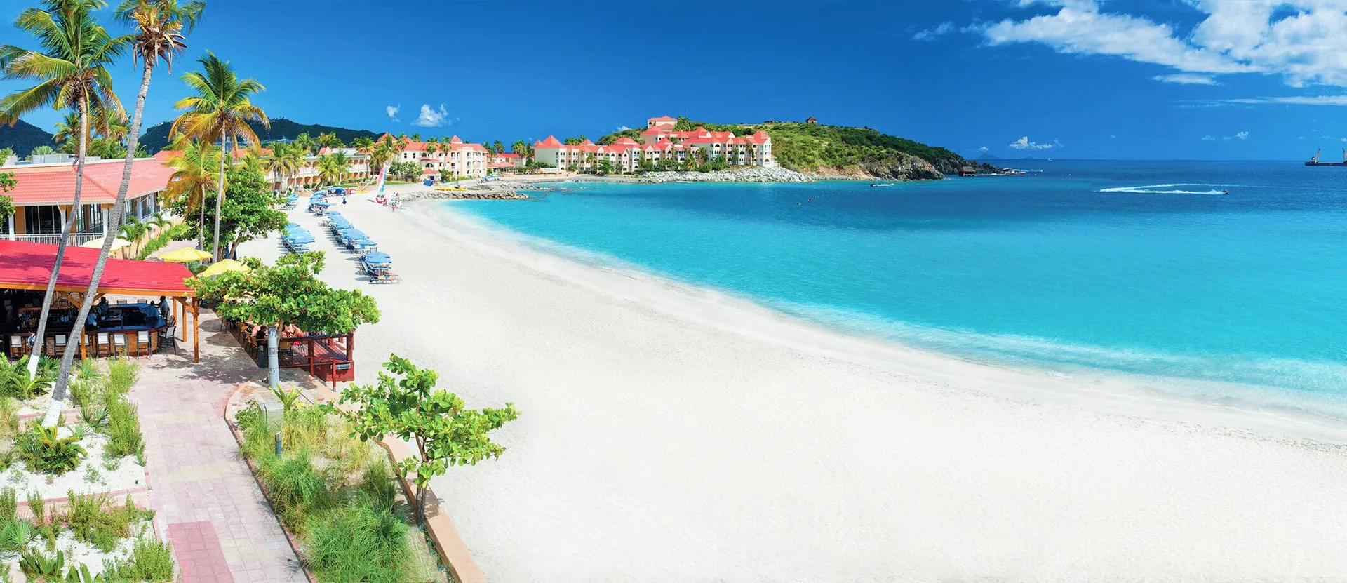 A panoramic beach view shows white sand and turquoise water at Divi Little Bay Beach Resort.