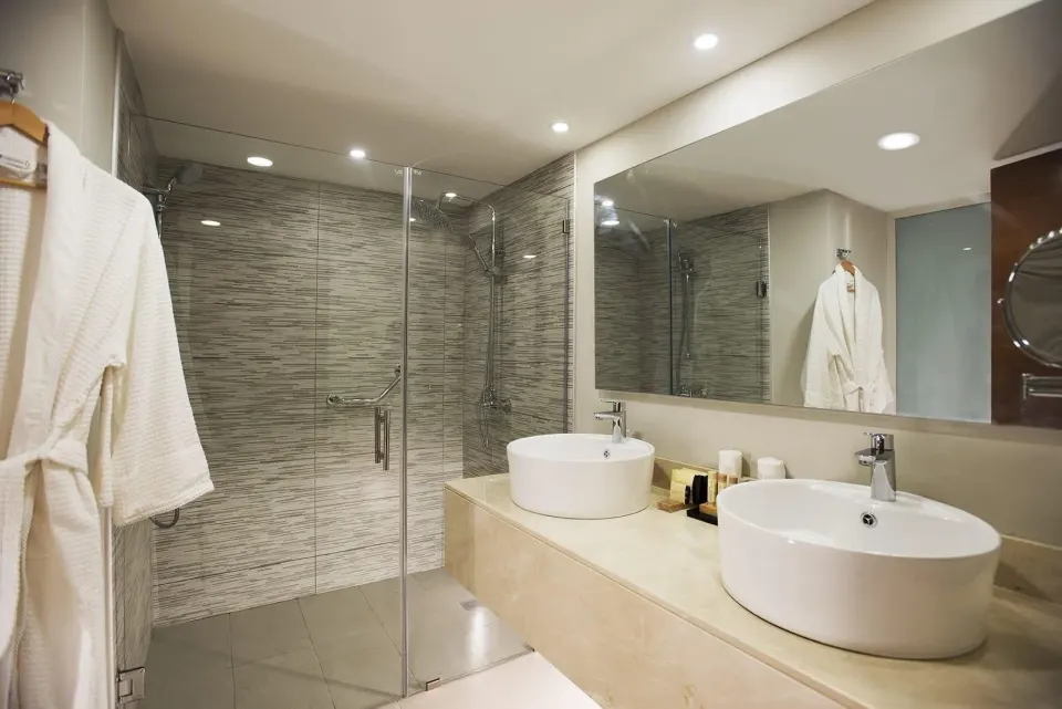 Superior Standard bathroom at Emotions by Hodelpa Puerto Plata with double sinks, glass shower, and bathrobe.