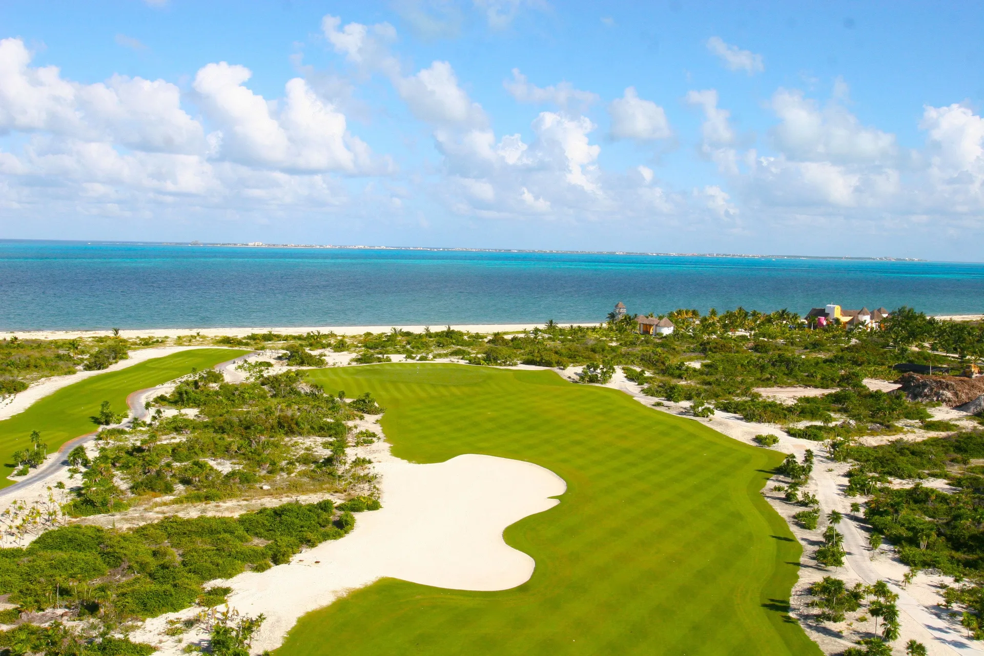 Aerial view of a coastal golf fairway and turquoise sea at Excellence Playa Mujeres.