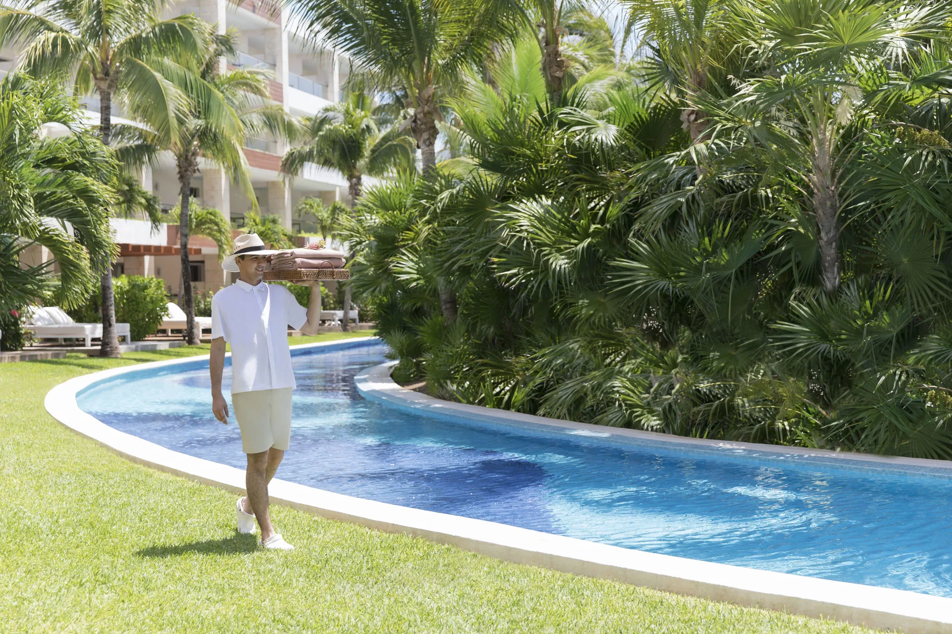 Staff member carrying towels beside a curving pool at Excellence Playa Mujeres.