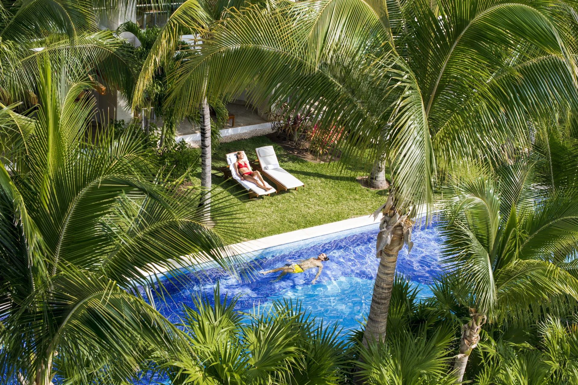 Guest floating in a narrow pool framed by palm trees at Excellence Playa Mujeres.