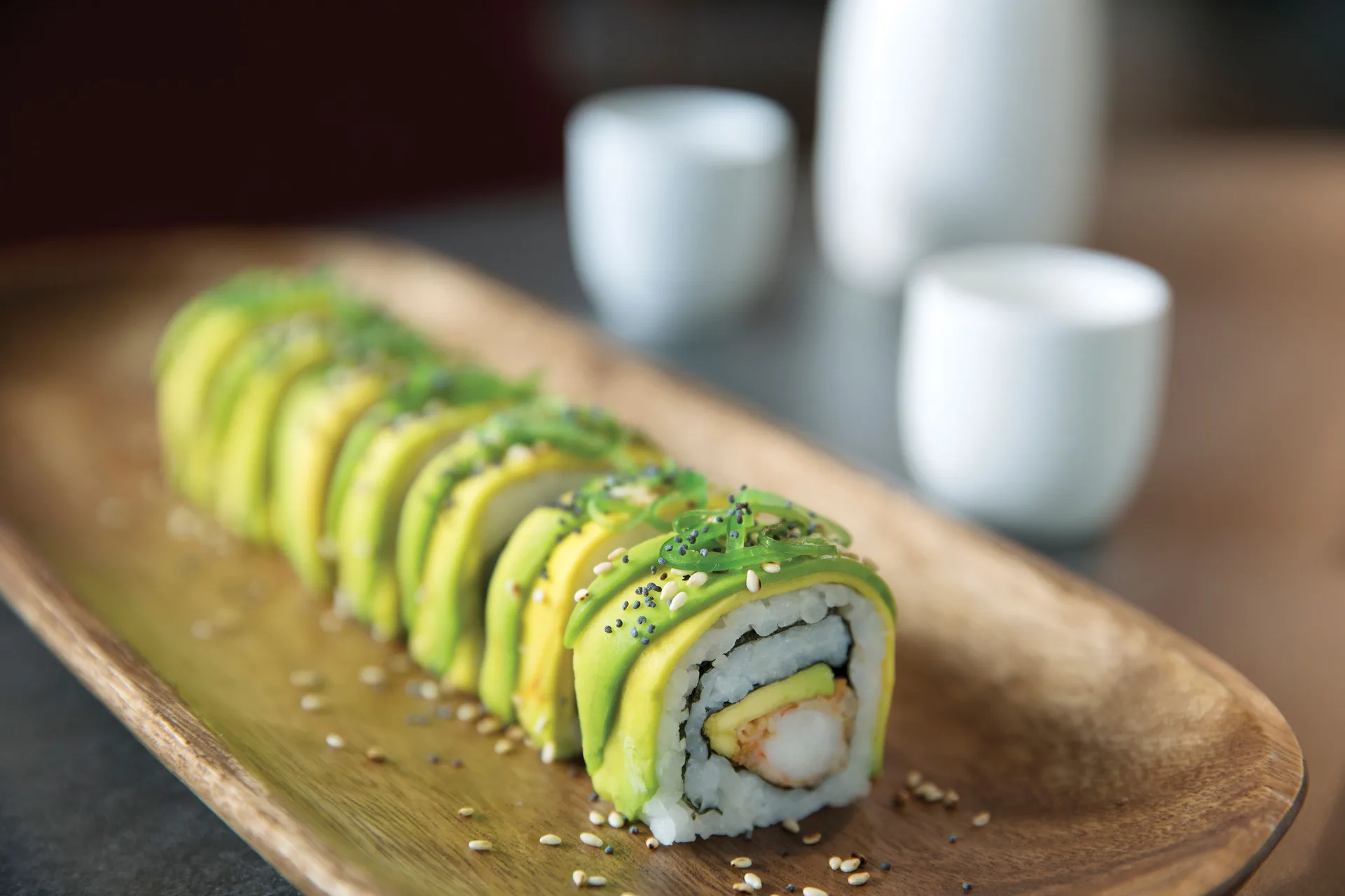 An avocado-topped sushi roll is served on a wooden plate at Excellence Playa Mujeres.