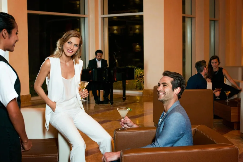 Guests with cocktails in a lounge with piano music at Excellence Playa Mujeres.