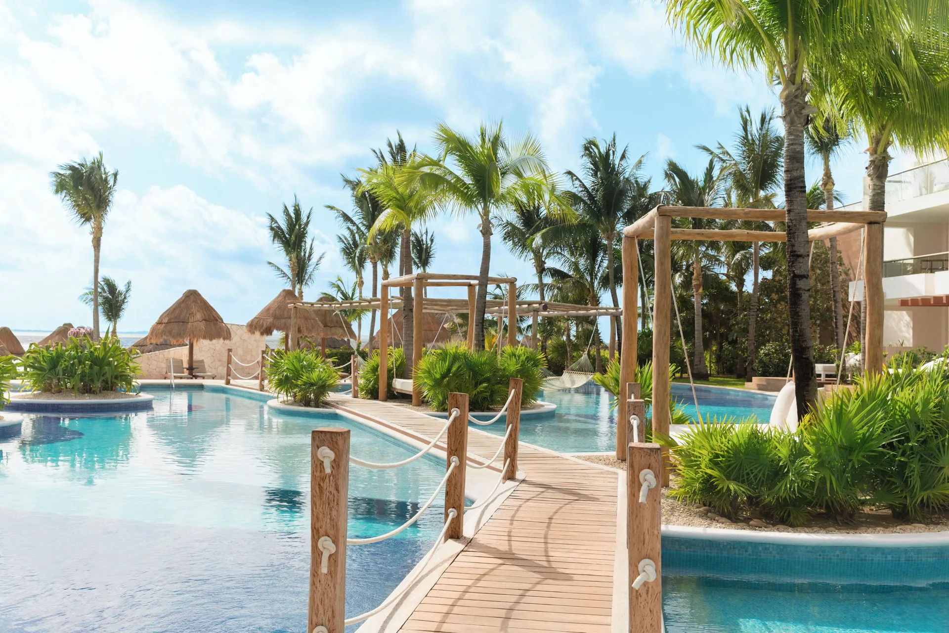Pool area with wooden bridge, hammocks, palms, and cabanas at Excellence Playa Mujeres.