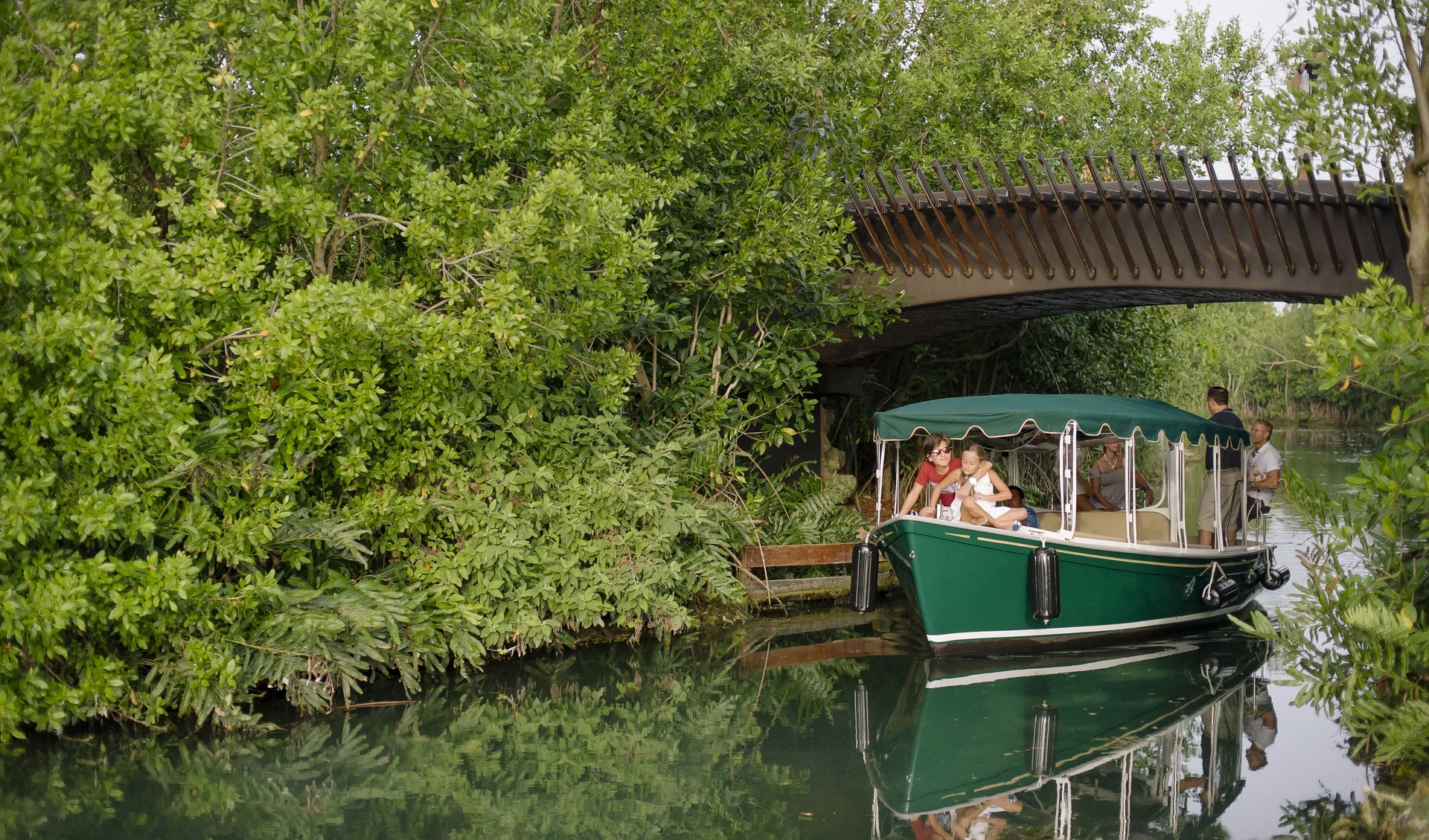 A covered boat carries guests along a green canal at Fairmont Heritage Place Mayakoba.