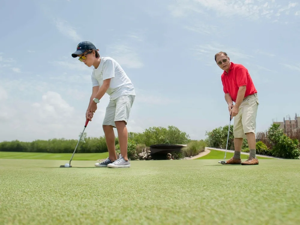 Two guests putt on a golf green under a pale sky at Fairmont Heritage Place Mayakoba.
