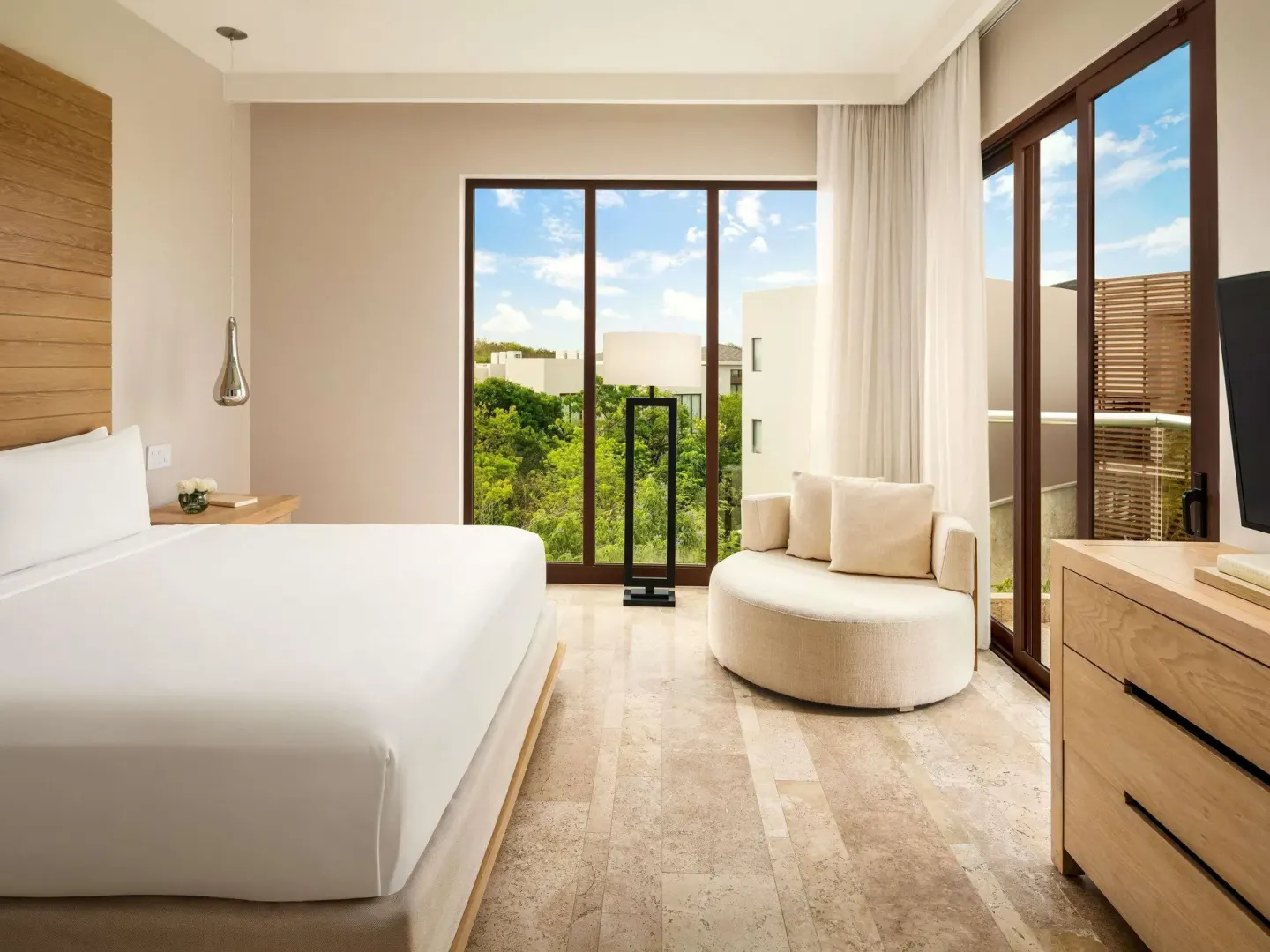 King bedroom with curved lounge chair and balcony doors at Fairmont Heritage Place Mayakoba.
