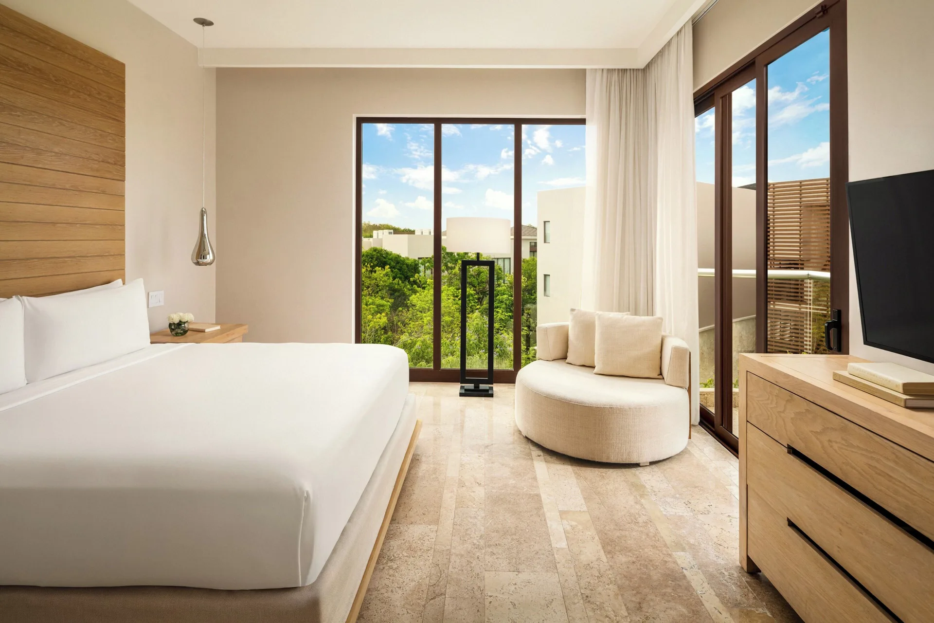 King bedroom with balcony windows and round lounge chair at Fairmont Heritage Place Mayakoba.