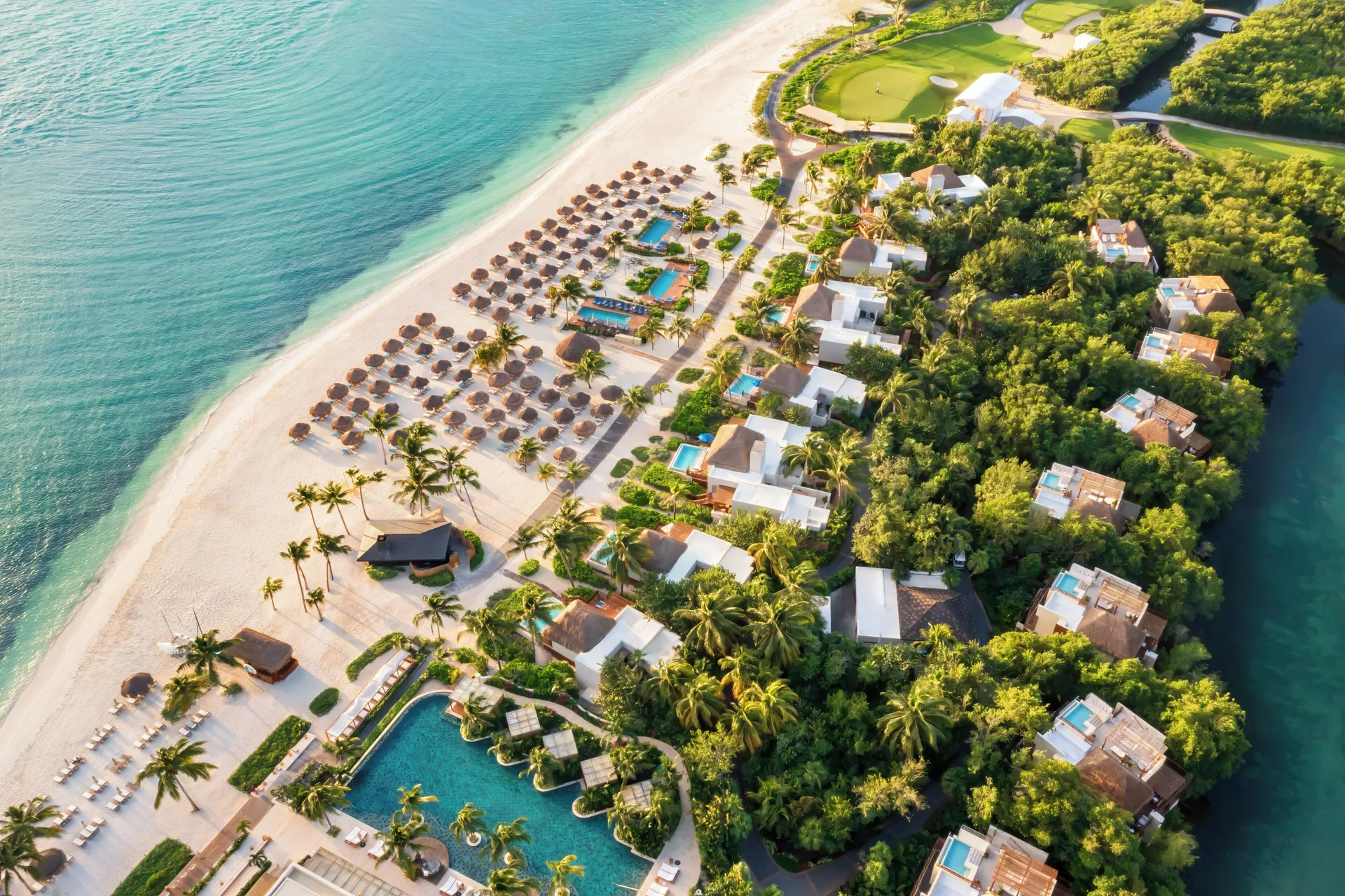 Aerial view of the beachfront buildings, pools, palms, and sand at Fairmont Mayakoba.
