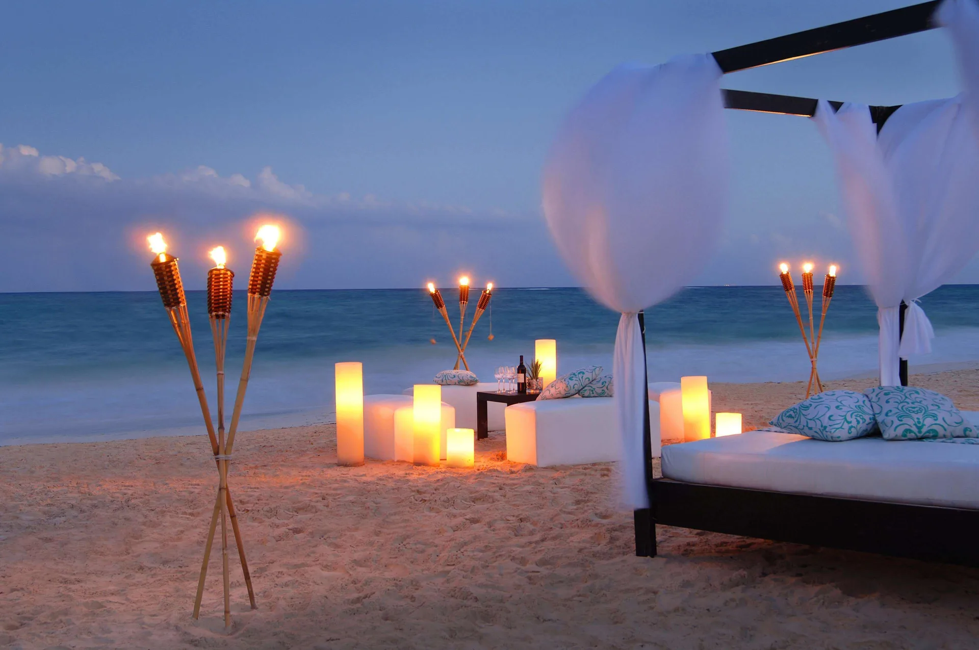 Beach lounge bed with torches and glowing lanterns by the sea at Fairmont Mayakoba.