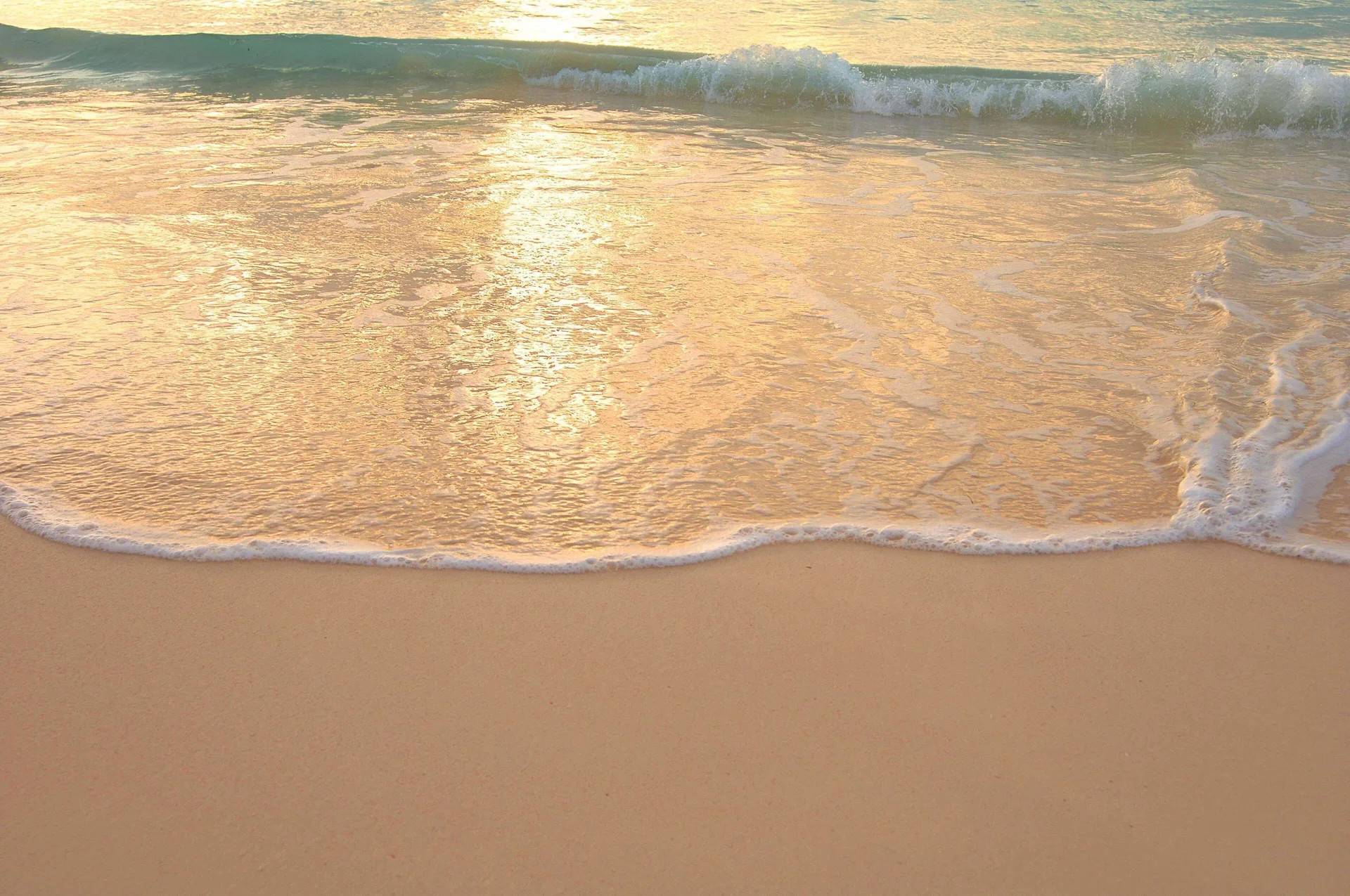 Golden light reflects on gentle waves washing over the beach at Fairmont Mayakoba.