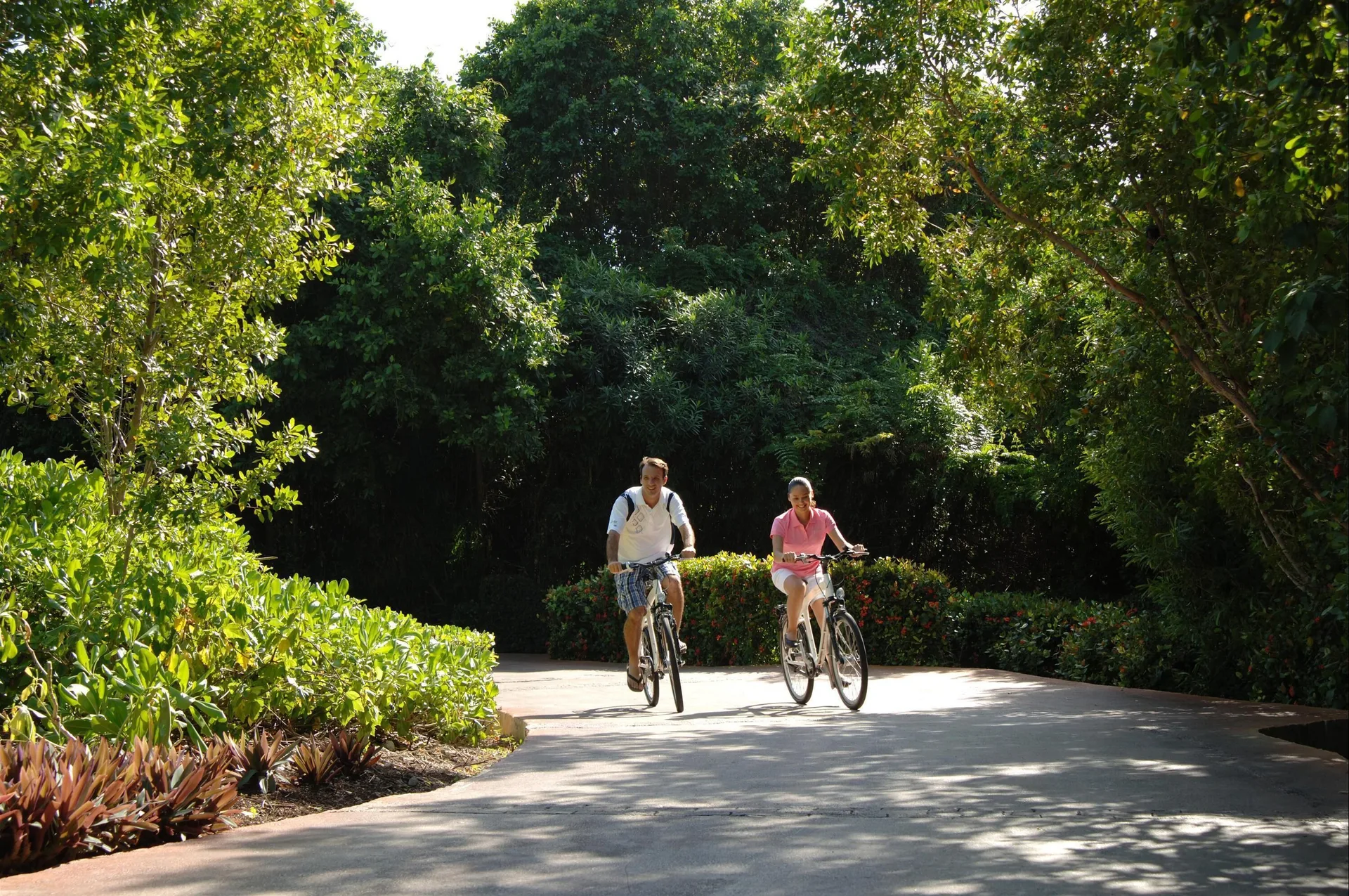 Two guests cycling along a shaded garden path at Fairmont Mayakoba.