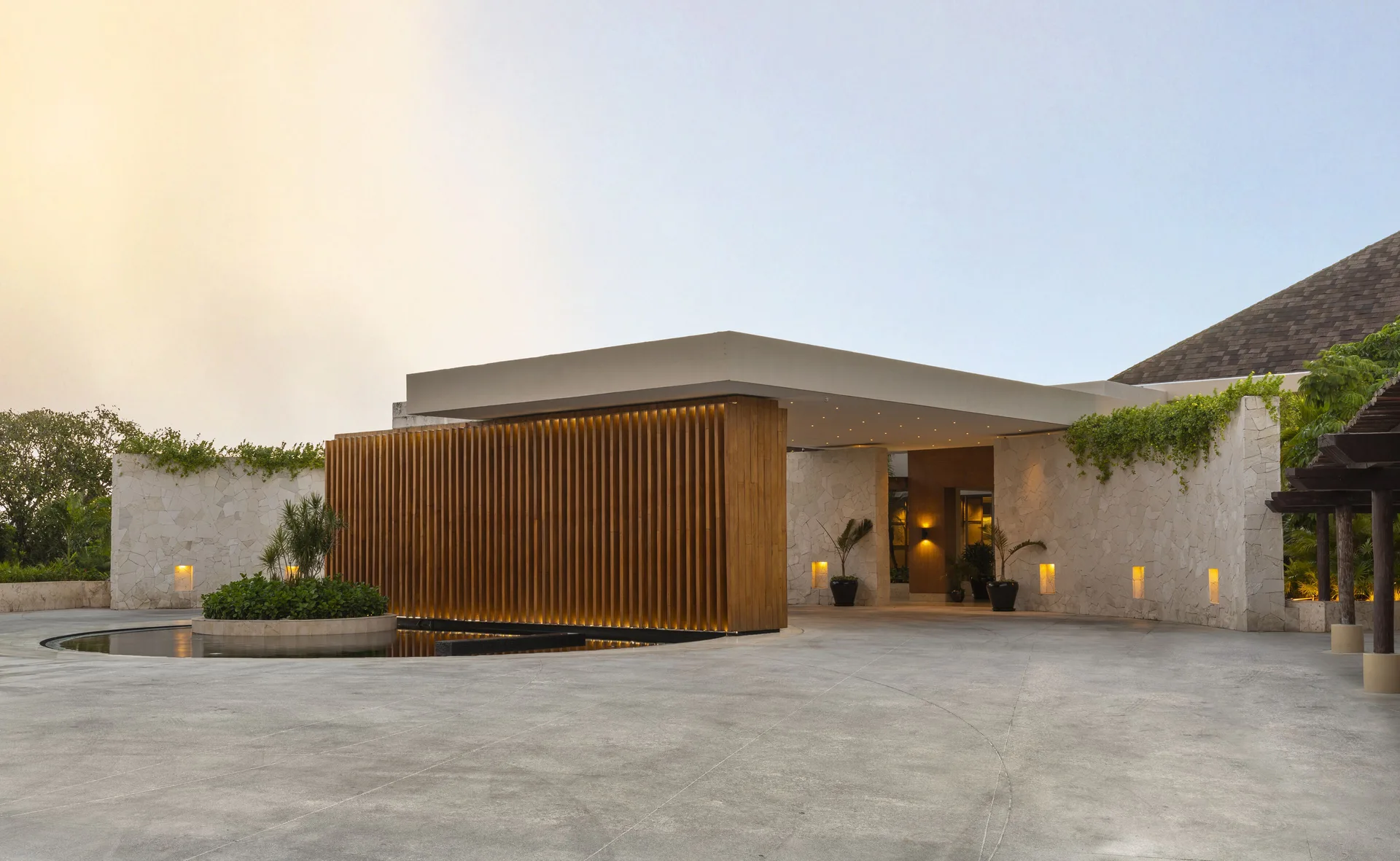 Modern stone and wood entrance building glows at dusk at Fairmont Mayakoba.