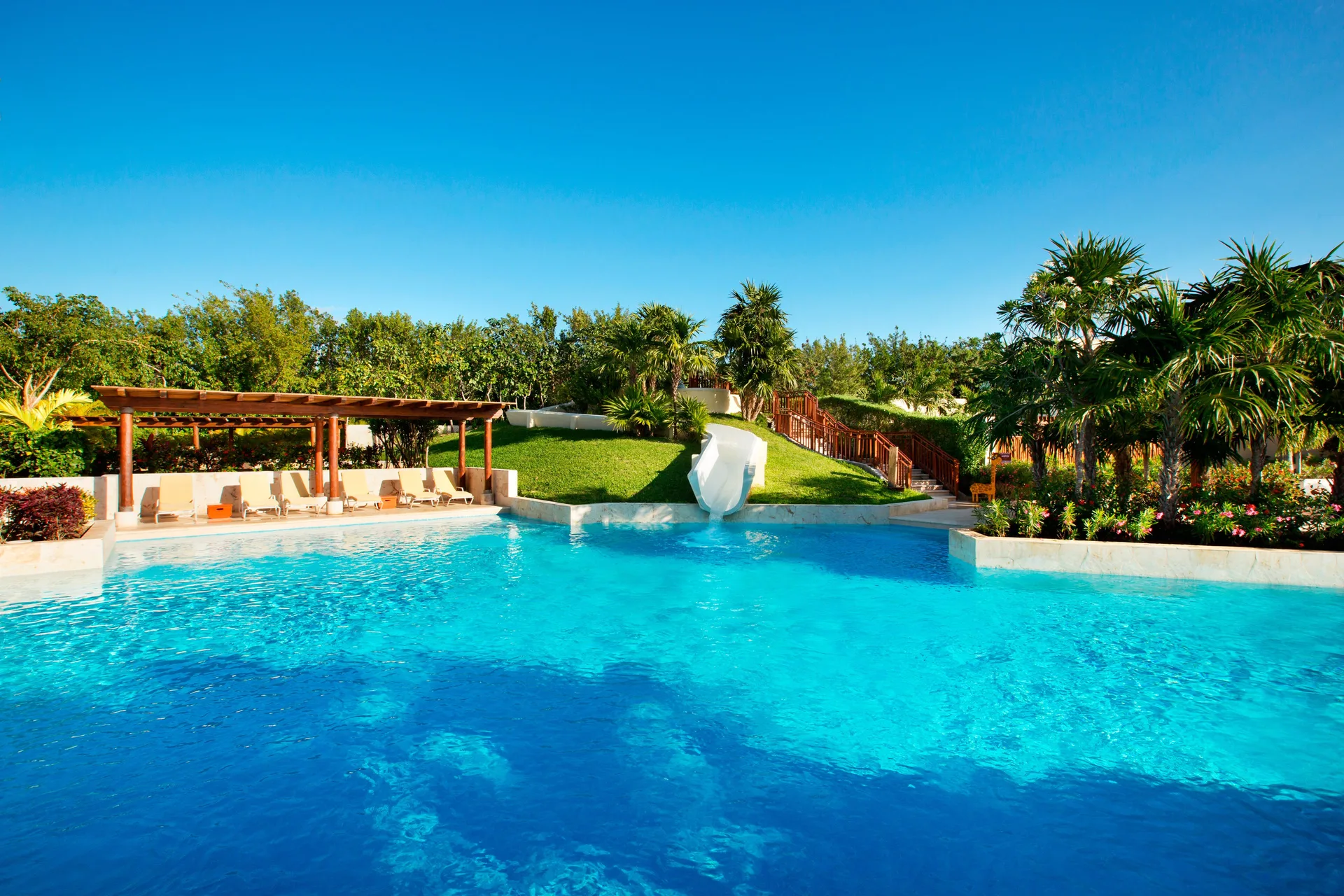 Large blue pool with a white slide, loungers and tropical gardens at Fairmont Mayakoba.