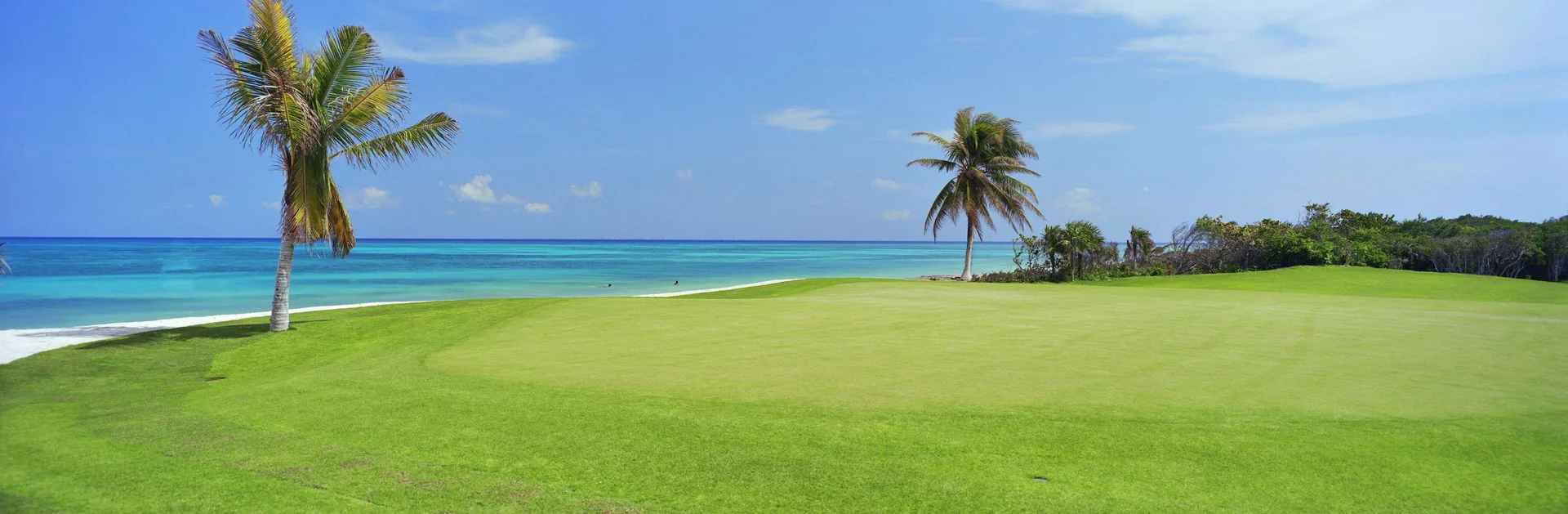 Seaside golf green with palm trees and blue ocean at Fairmont Mayakoba.