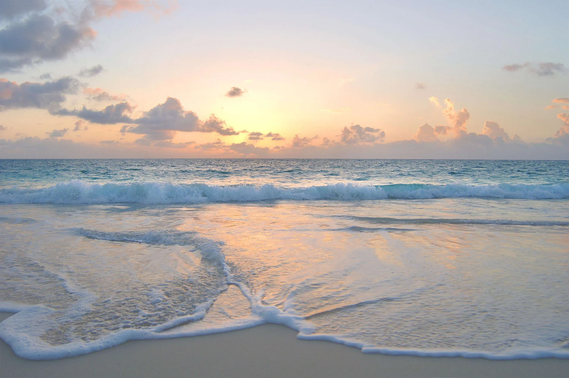 Sunrise colors the sky over waves and wet sand at Fairmont Mayakoba.