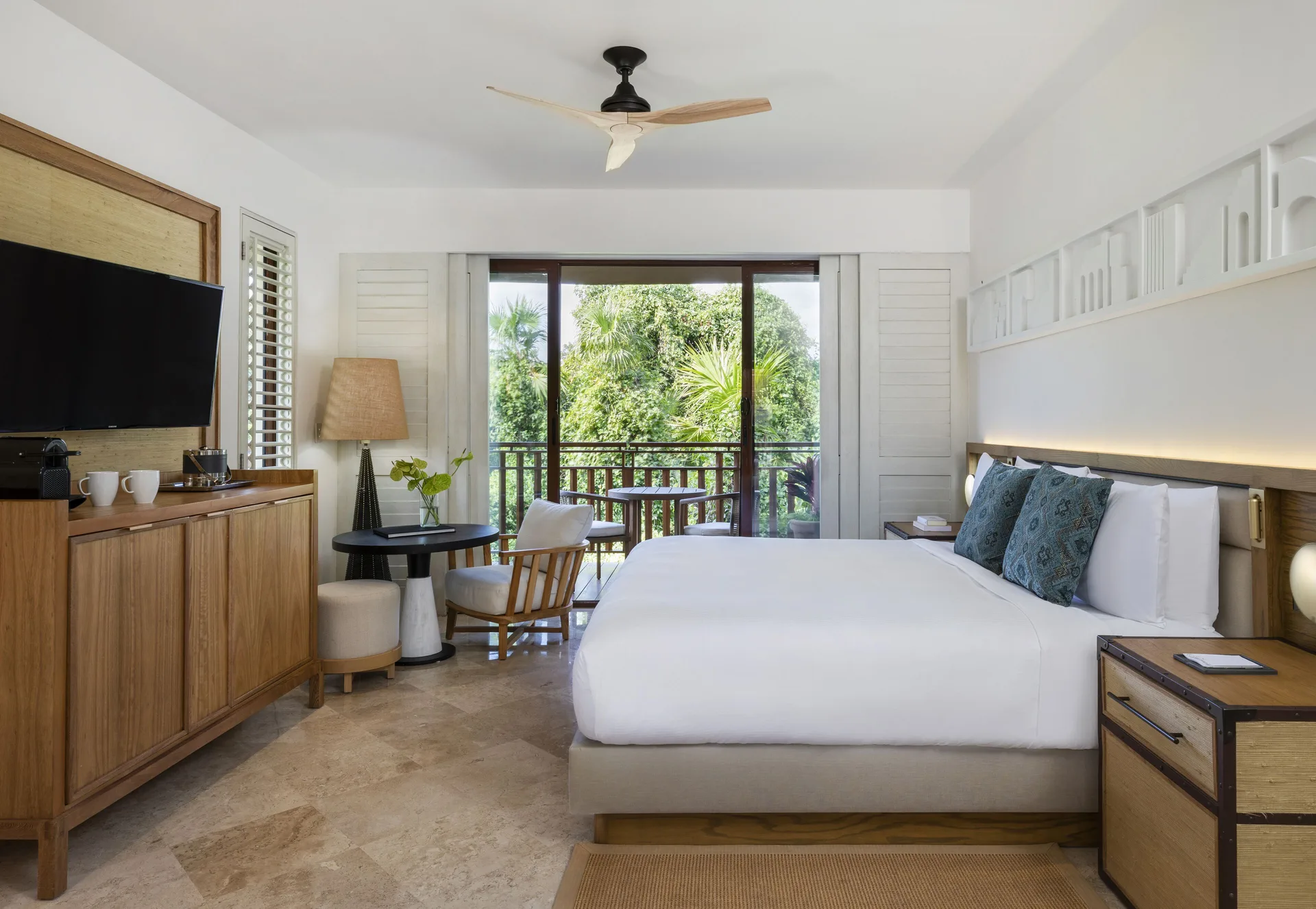 King bed in a Casita Deluxe Room at Fairmont Mayakoba with balcony seating and tropical greenery.