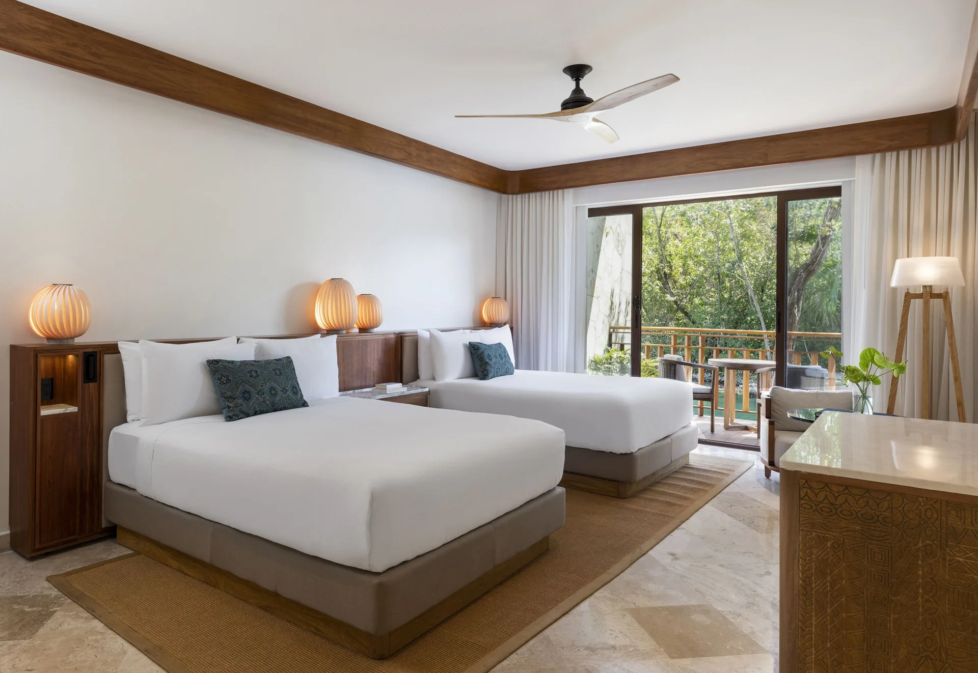 Two queen beds in a Casita Signature Room at Fairmont Mayakoba with a balcony facing trees.