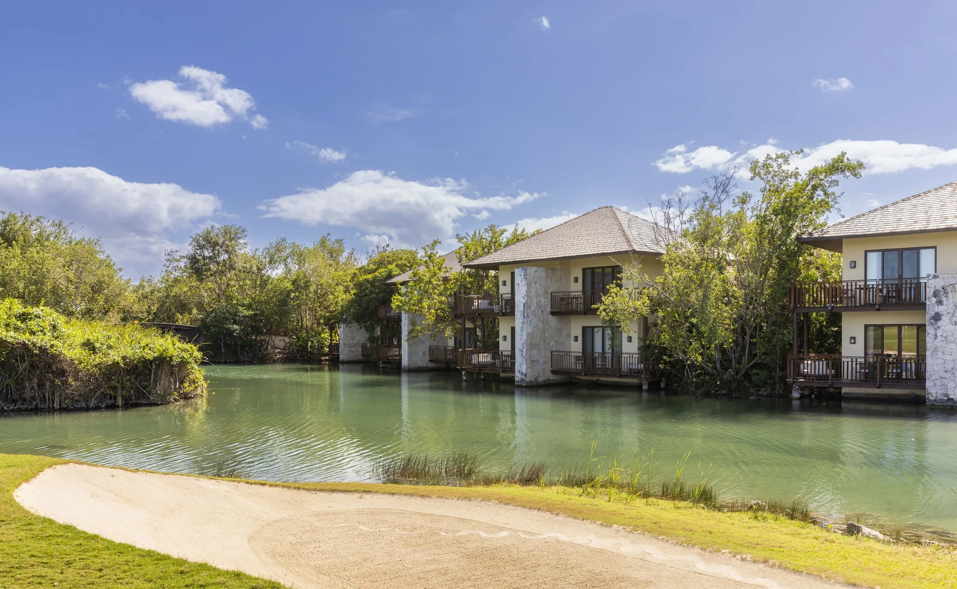 Canal-side casita buildings with balconies at Fairmont Mayakoba under a blue sky.