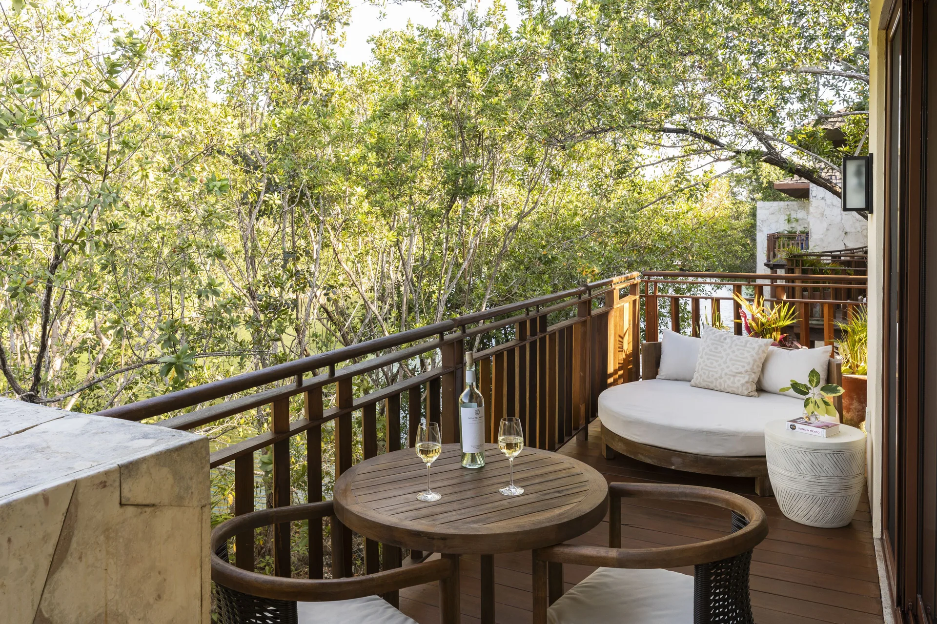 Canal-view terrace seating with daybed at Fairmont Mayakoba surrounded by trees.